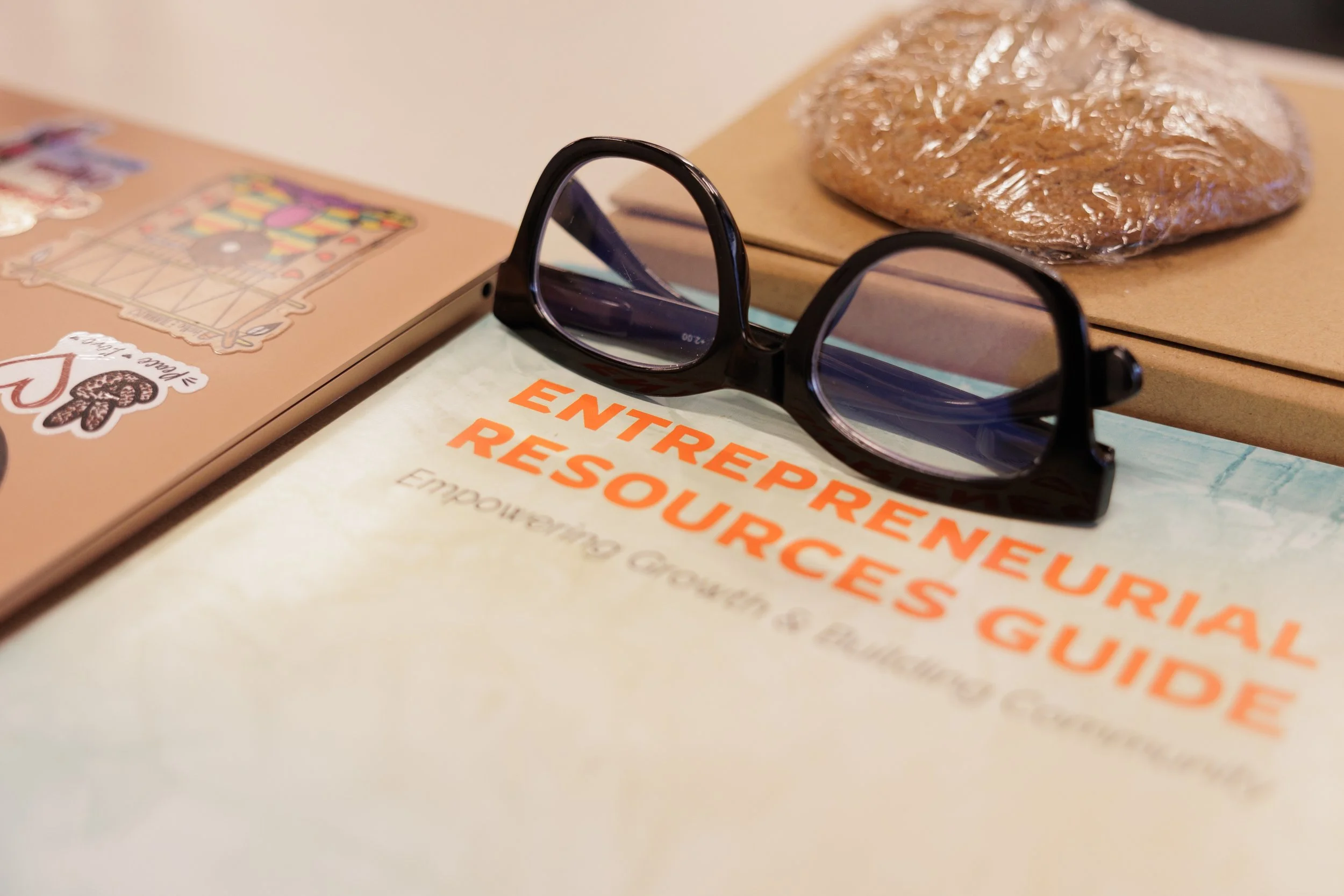 A man in a hat helping a young person with glasses work on a laptop at a table during a group activity or workshop.