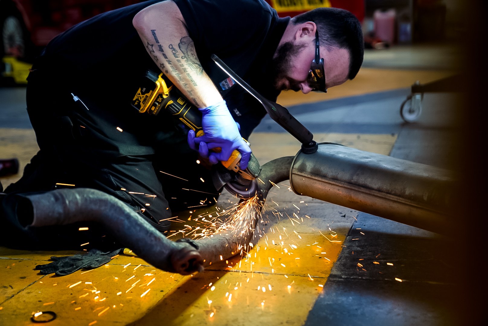 Mechanic cutting exhaust pipe with angle grinder, emitting sparks.