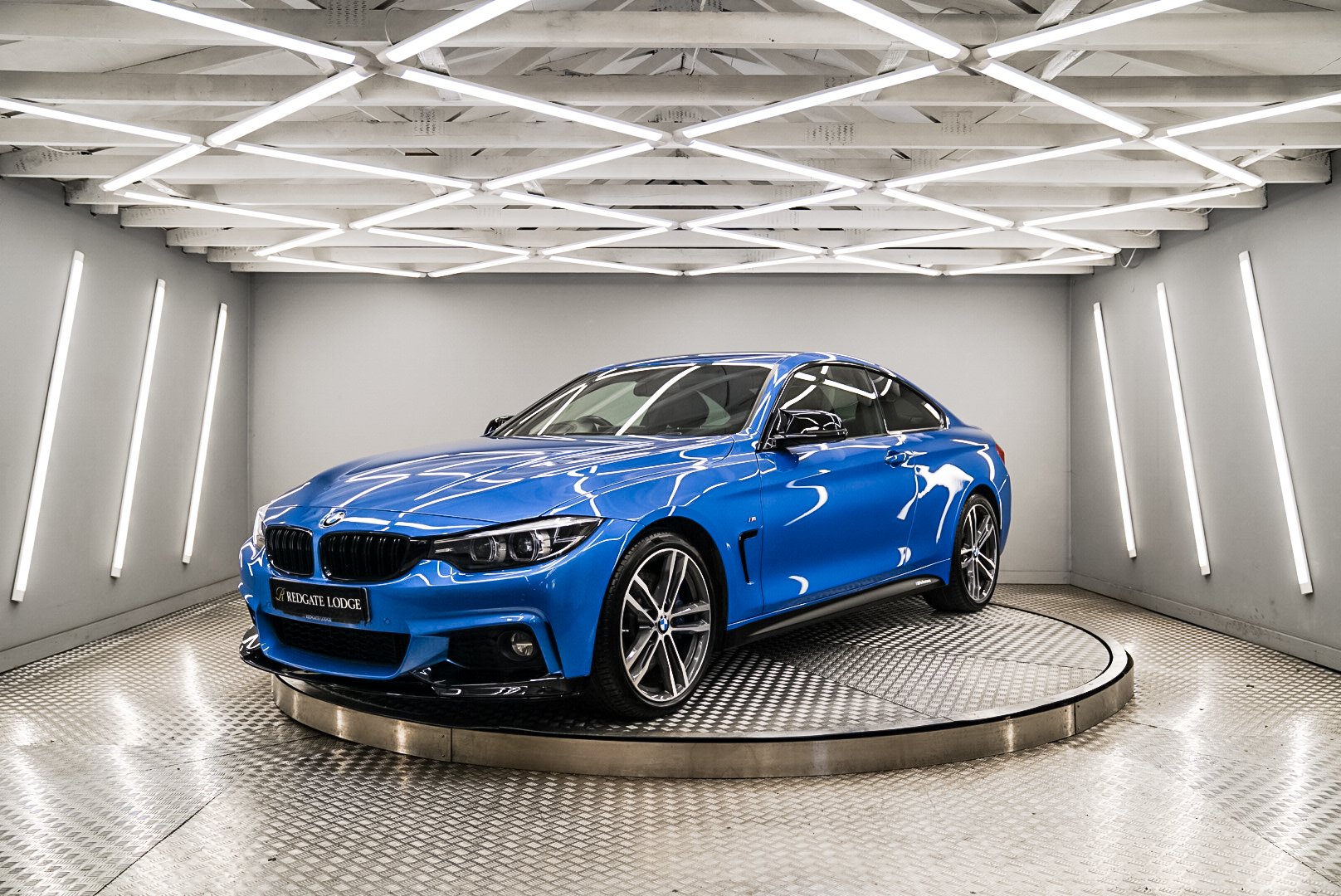 Blue BMW car on a rotating platform in a modern showroom with geometric lighting.