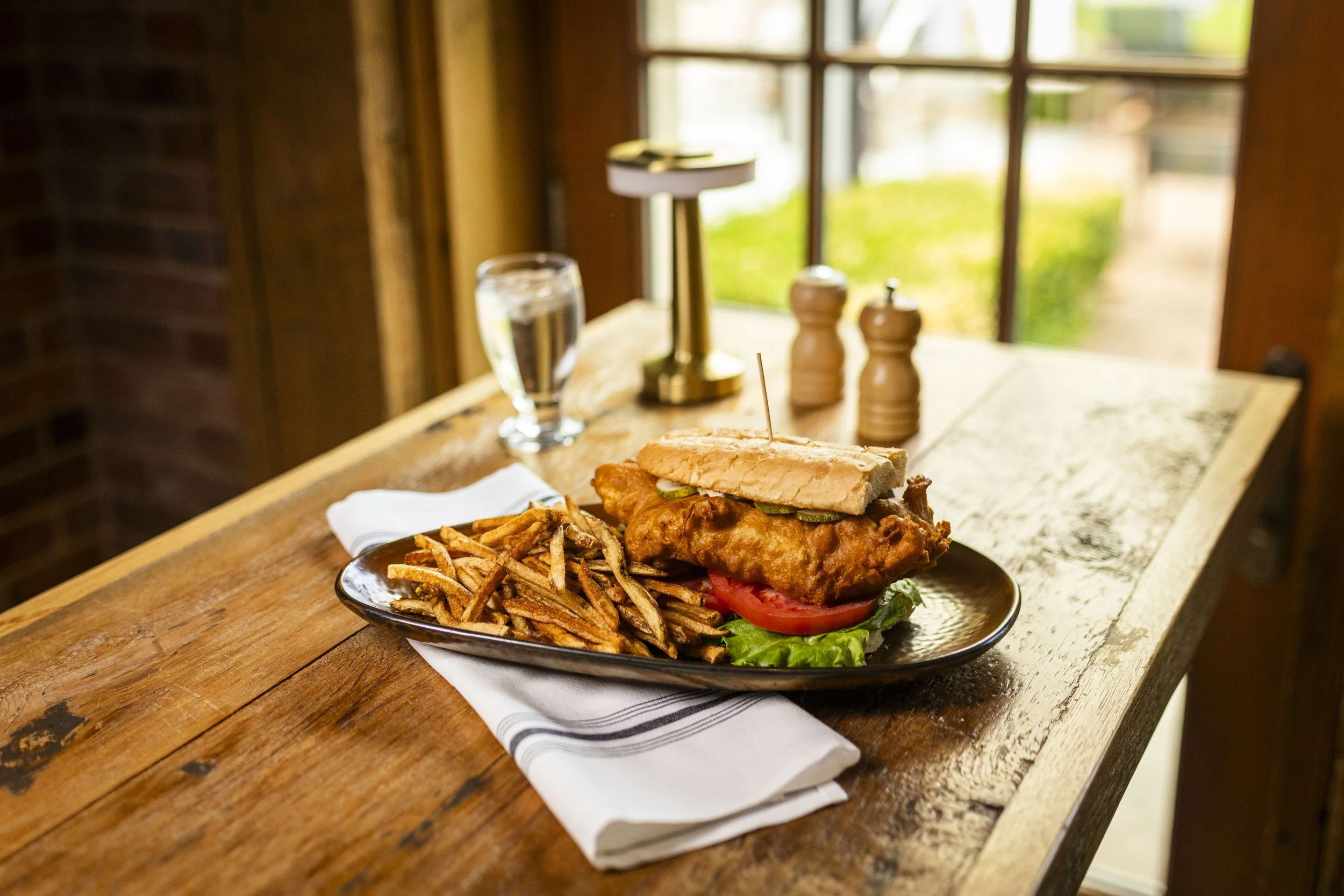Crispy fried fish sandwich with lettuce, tomato, pickles, and house-made tartar sauce at Peter Allen Inn