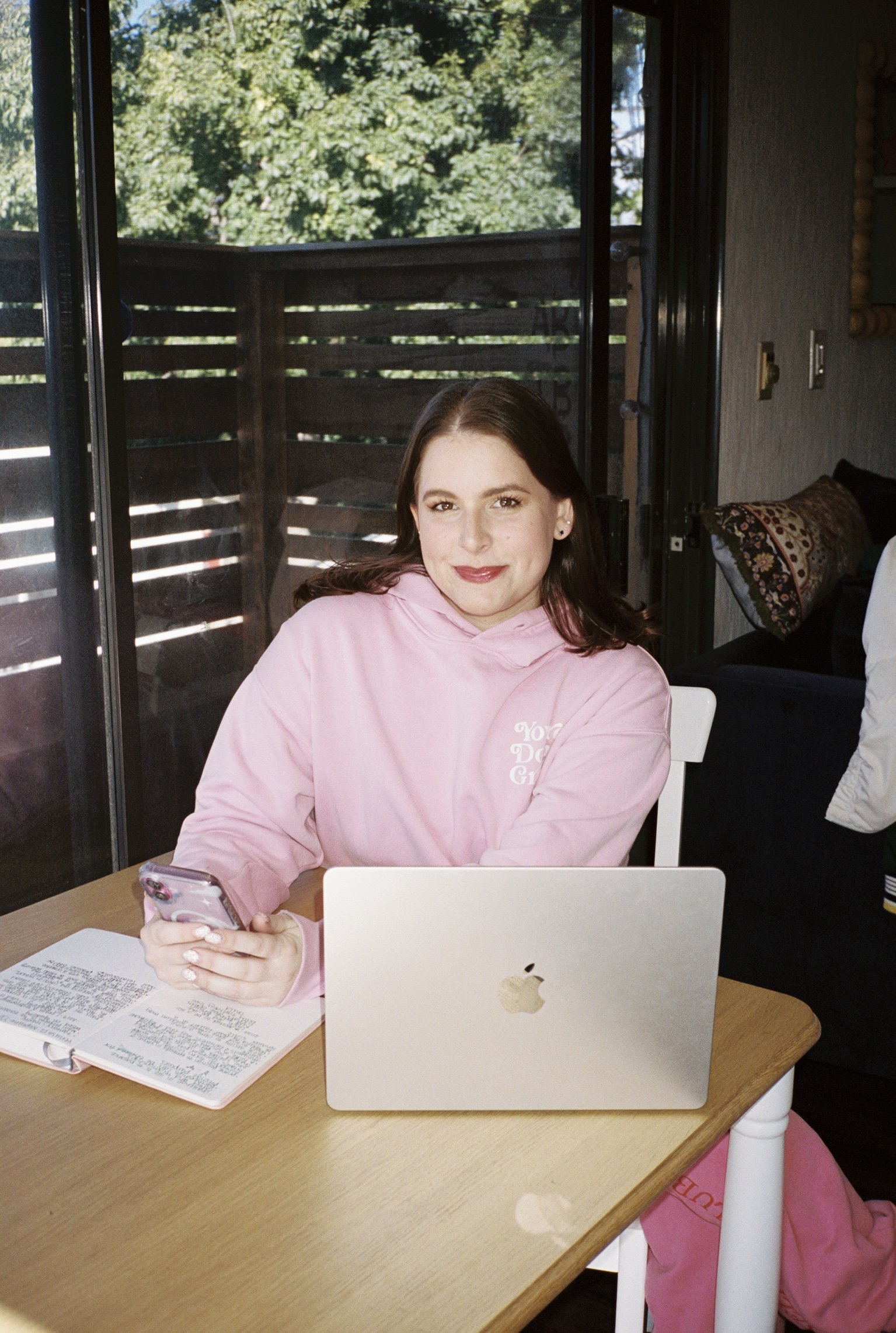 adri barnhardt, the astrologer behind lovingly, adri, smiling at her desk with her journal and laptop