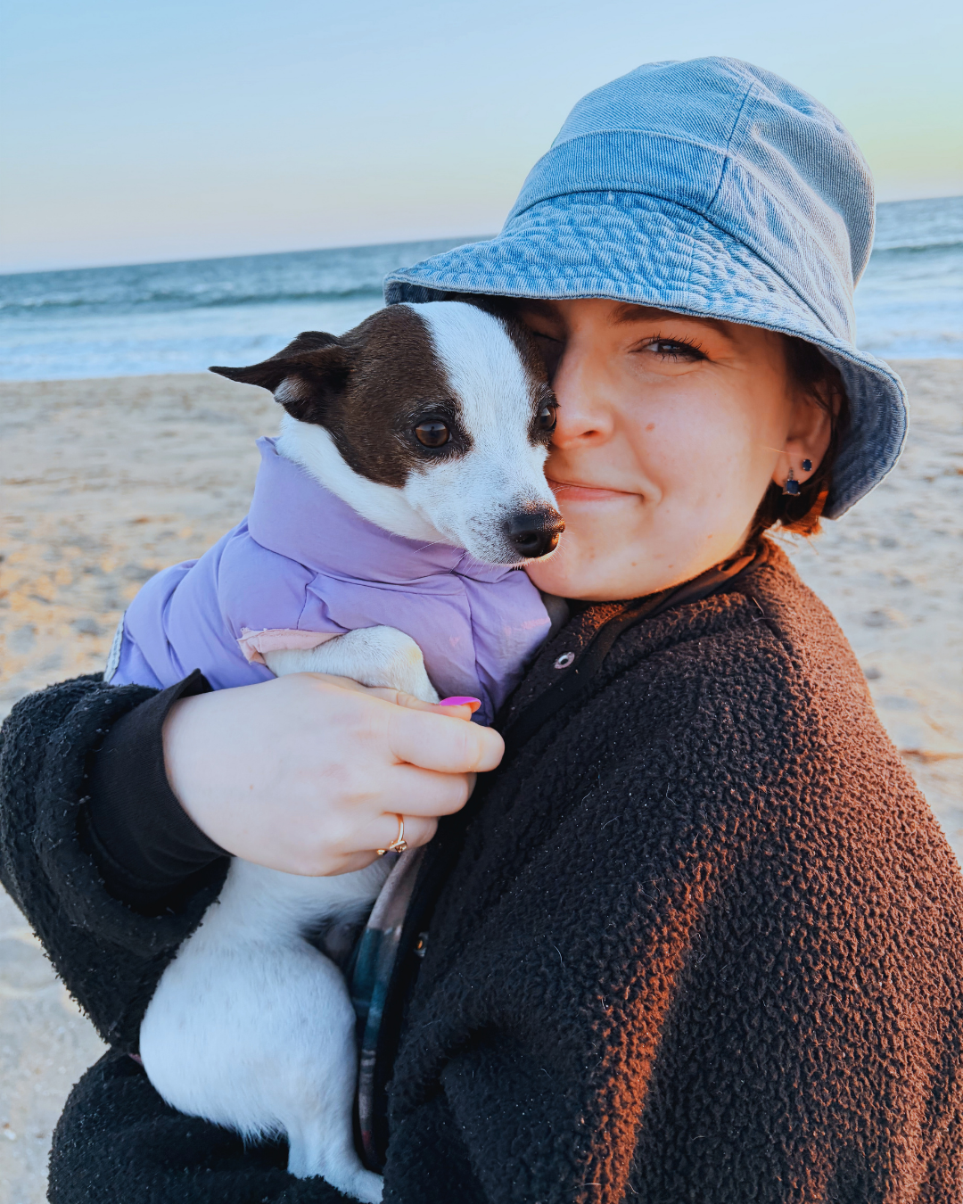 girl in a bucket hat on the beach at sunset with black and white chihuahua