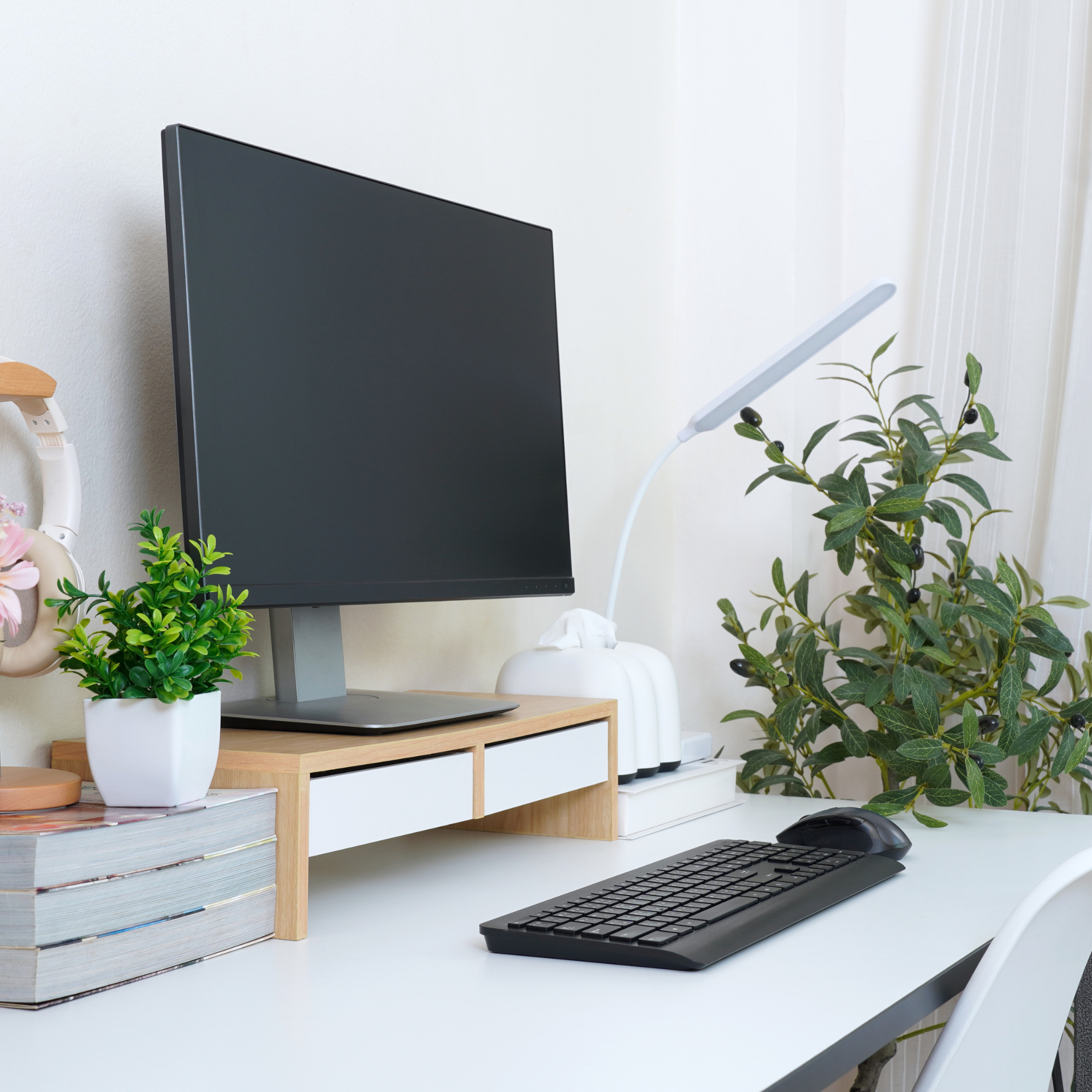 Home office desk with a computer monitor, keyboard, mouse, potted plants, a tissue box, and a small lamp.