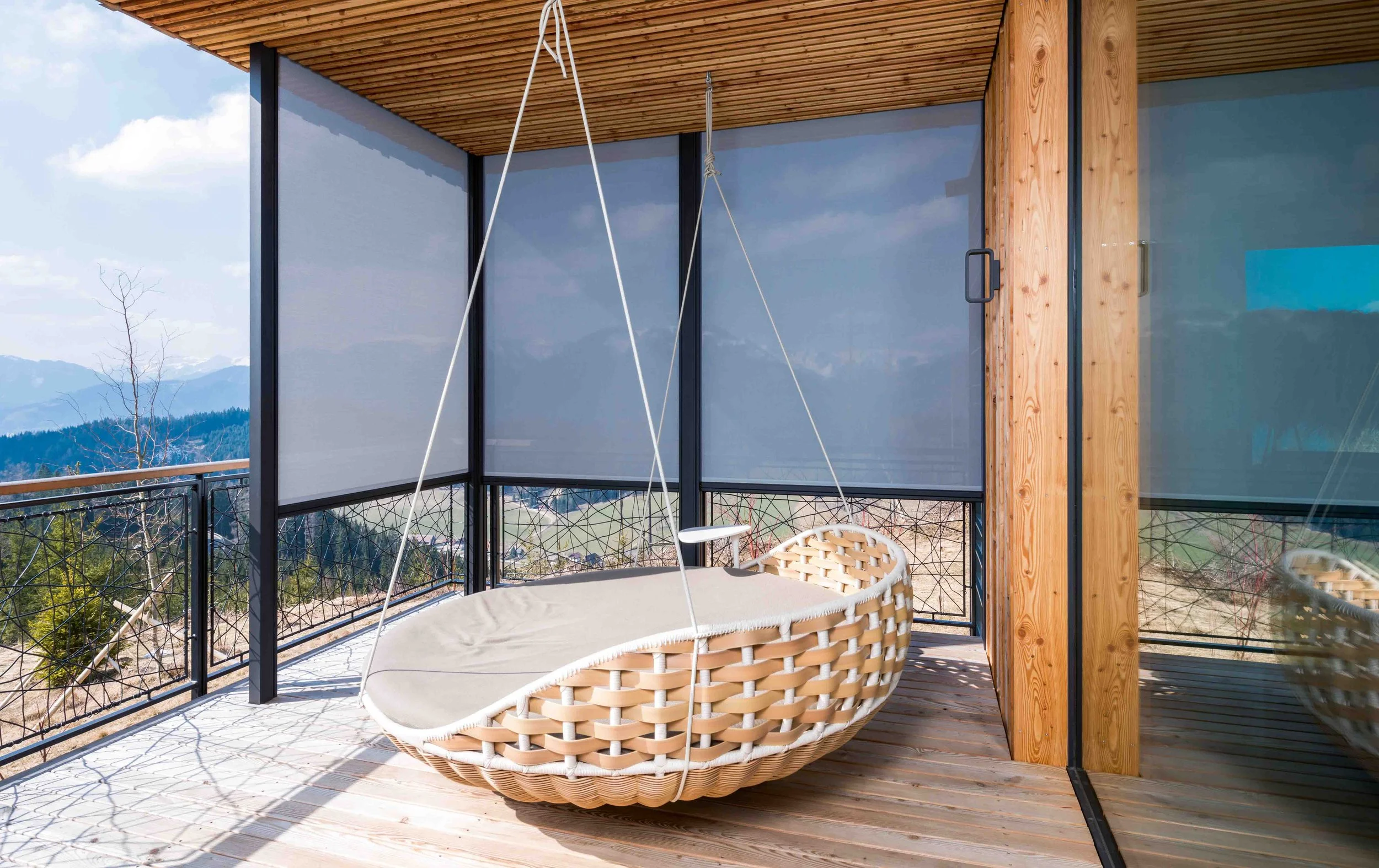 Ein Balkon mit einer schaukelnden Korbschaukel, umgeben von einem Zaun mit einer schönen Berglandschaft im Hintergrund.