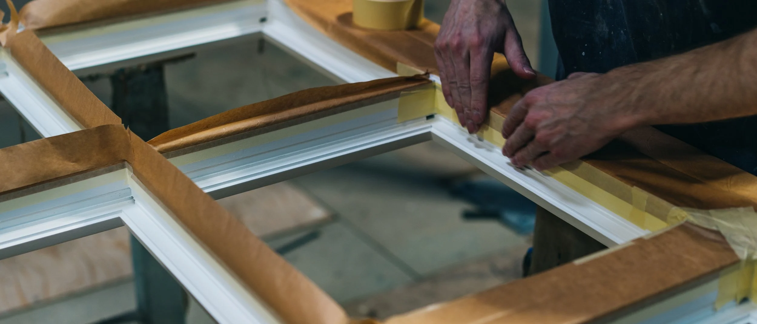 Eine Person arbeitet an einem Rahmen für ein Fenster oder eine Tür, der sorgfältig mit Klebeband und Papier geschützt wird.