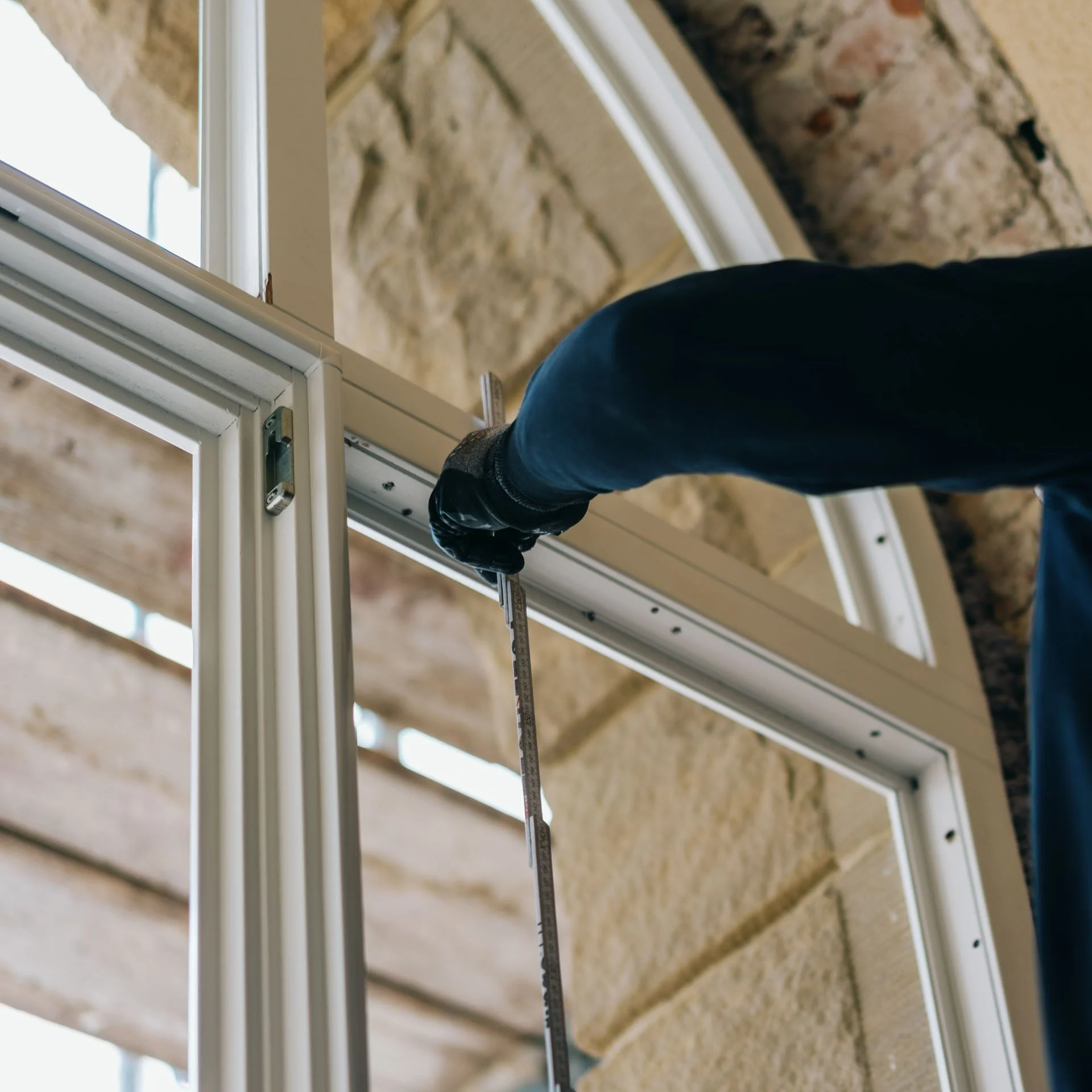 Ein Handwerker installiert ein Fensterrahmen in einem Haus mit Steinwand, misst den Rahmen mit einem Lineal.