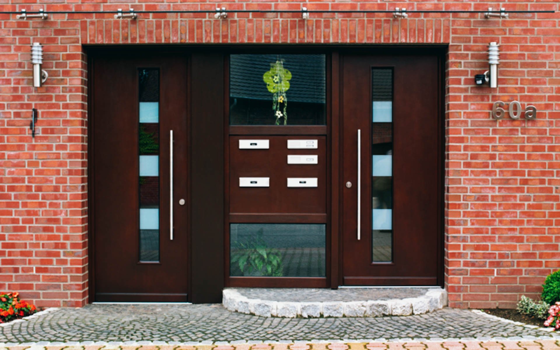 Hauseingang mit doppelter Holztür, Fenster, Briefkästen und Hausnummer 60a vor einer roten Ziegelwand.