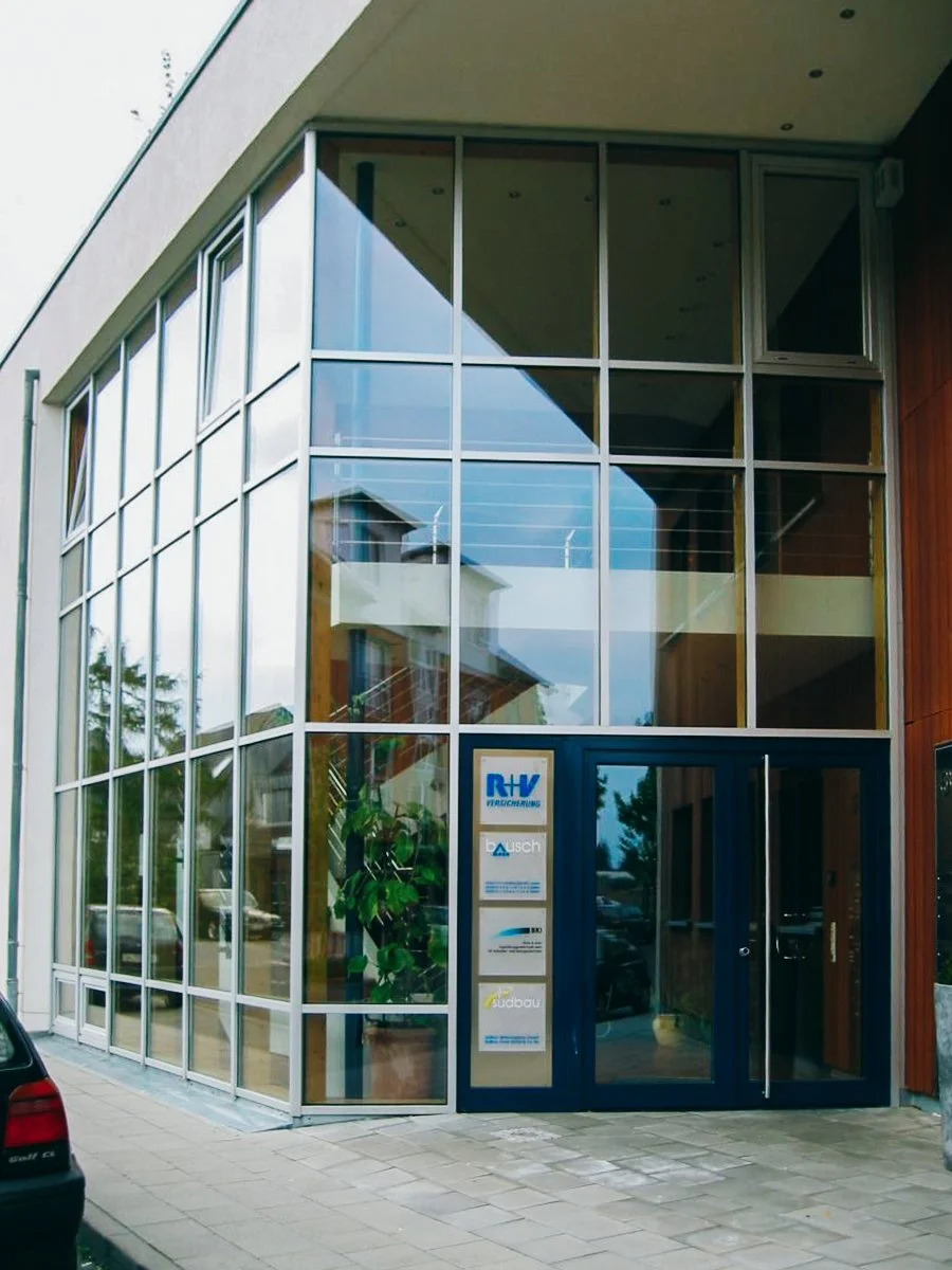 Modernes Geschäftsgebäude mit großen Glasfenstern und mehreren Unternehmensschildern am Eingang.