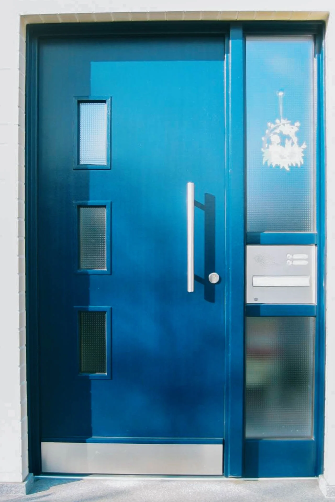 Blaue Haustür mit drei kleinen Fensterflächen, einem silbernen Türklinke, Briefkasten und einer Klingel