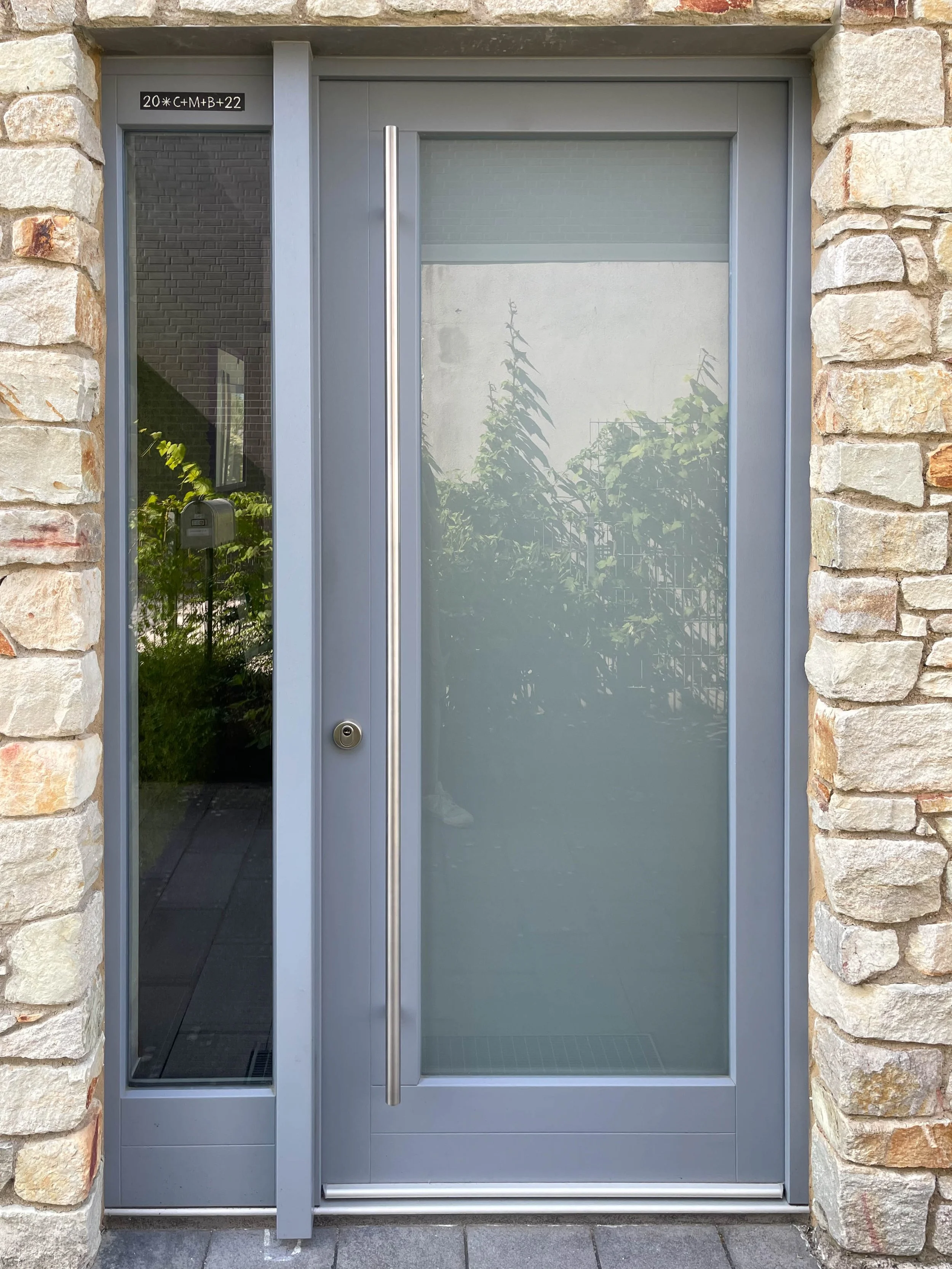 Moderner Eingangstür mit Glas und Steinmauer im Hintergrund.