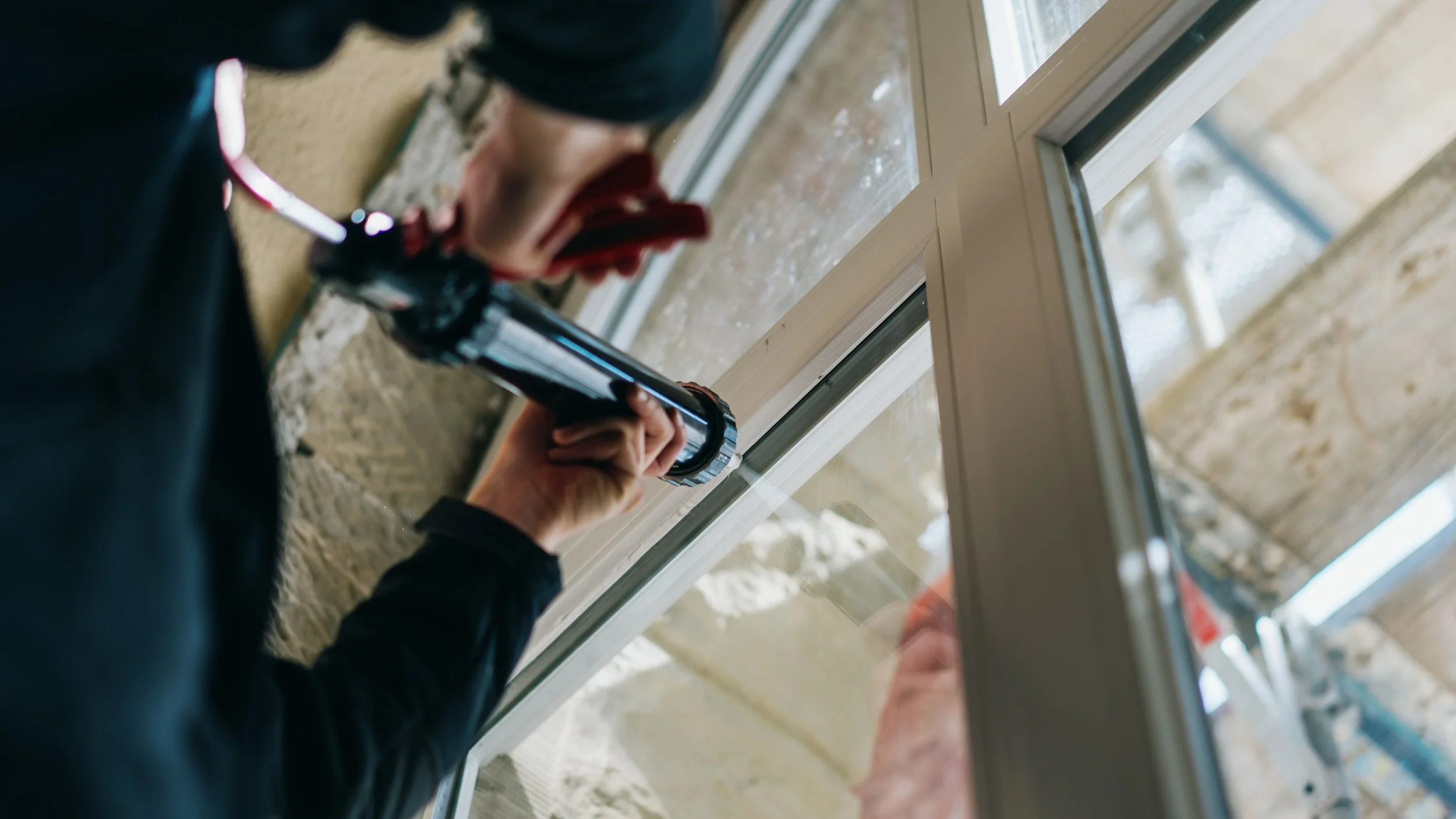 Handwerker legt Silikon in die Fuge zwischen Fensterrahmen und Wand.