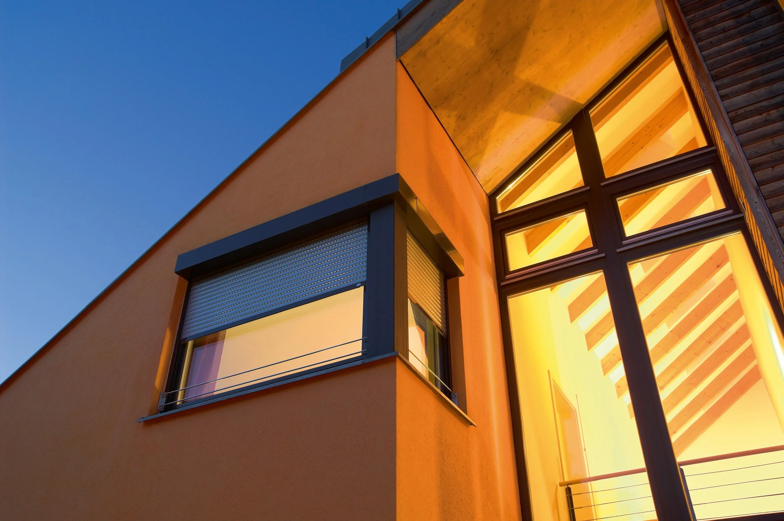 Moderne Architektur eines Hauses bei Sonnenuntergang, mit großen Fenstern und warmem Innenlicht.