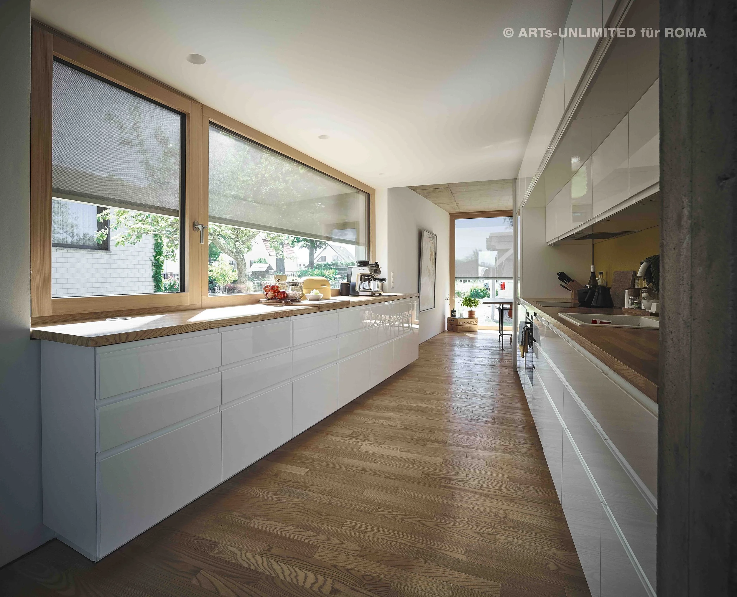 Moderne helle Küche mit Holzarbeitsplatten, große Fenster frontale Blick auf einen Garten, weiße Schränke, Holzdielenboden, kleine Küchengeräte und Dekorationen auf der Arbeitsplatte, natürliche Beleuchtung.