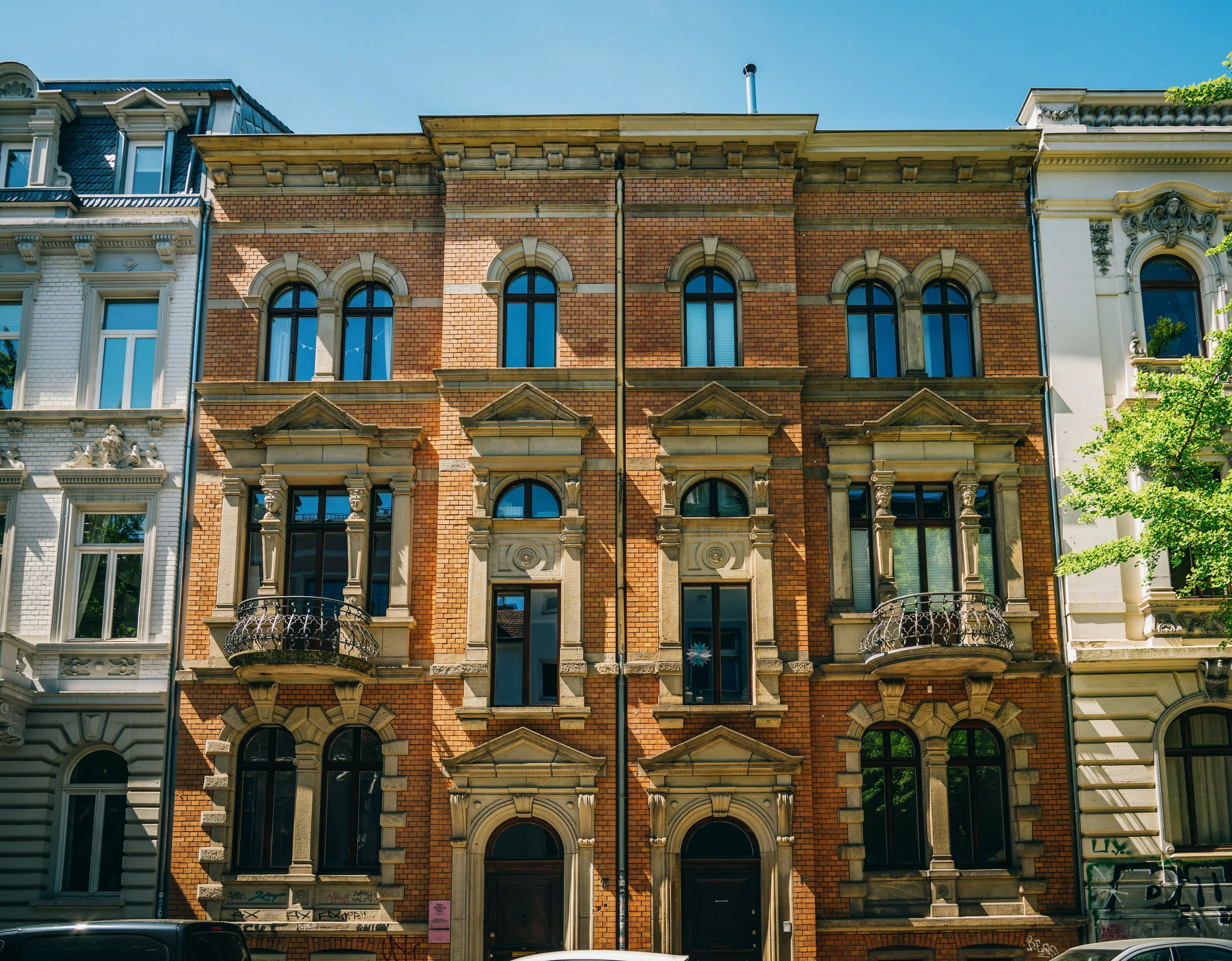 Mehrstöckiges historisches Gebäude mit rotem Backstein und archtop Fenstern, einige mit kleinen Balkonen, in einer Stadtstraße bei Sonnenschein.