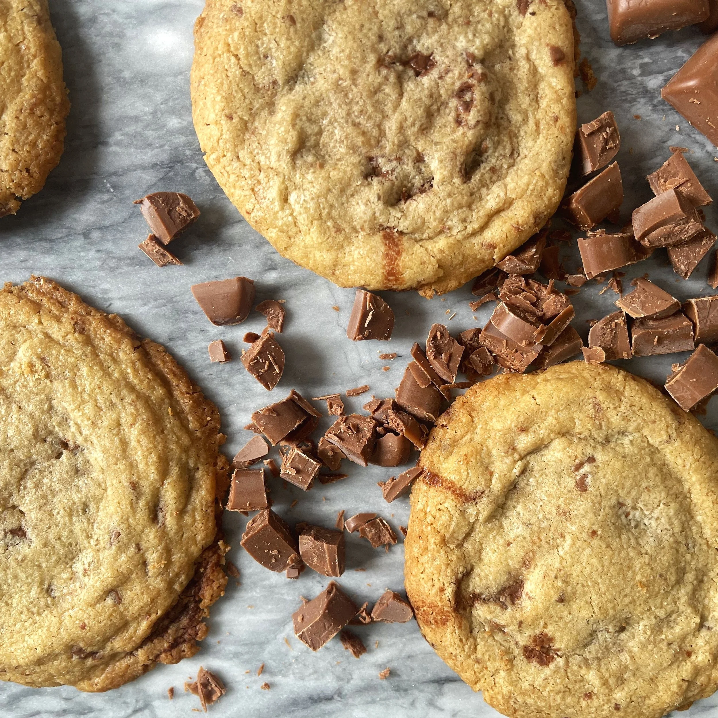 Chocolate chip cookies on marble surface with chopped chocolate pieces scattered around