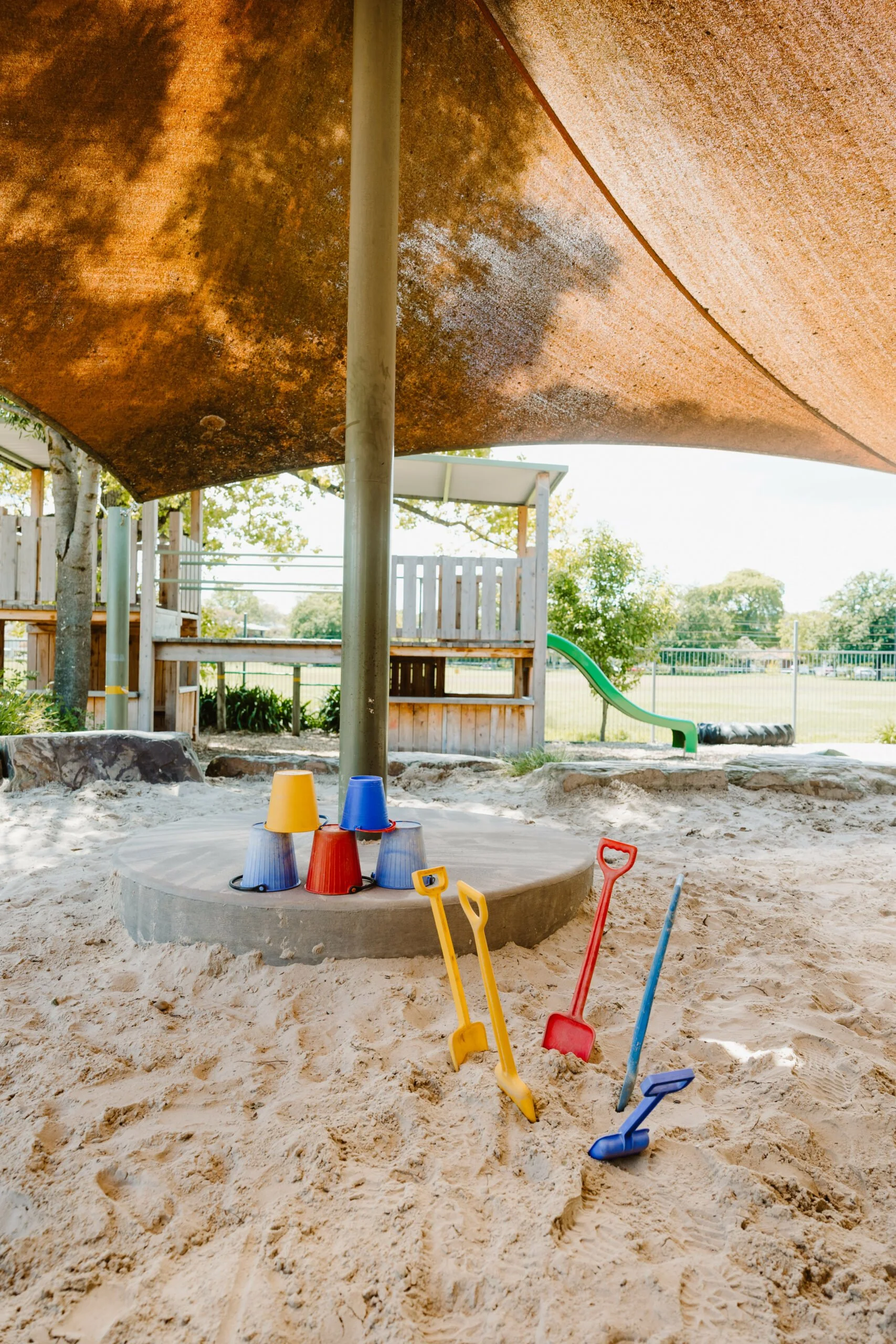 Sand-filled sandbox with colorful buckets and shovels at a playground.