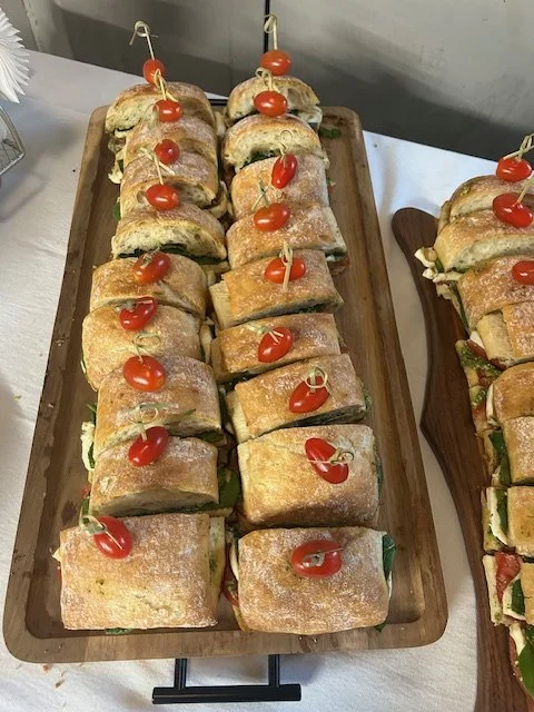 Assorted sandwiches with cherry peppers on a wooden tray.
