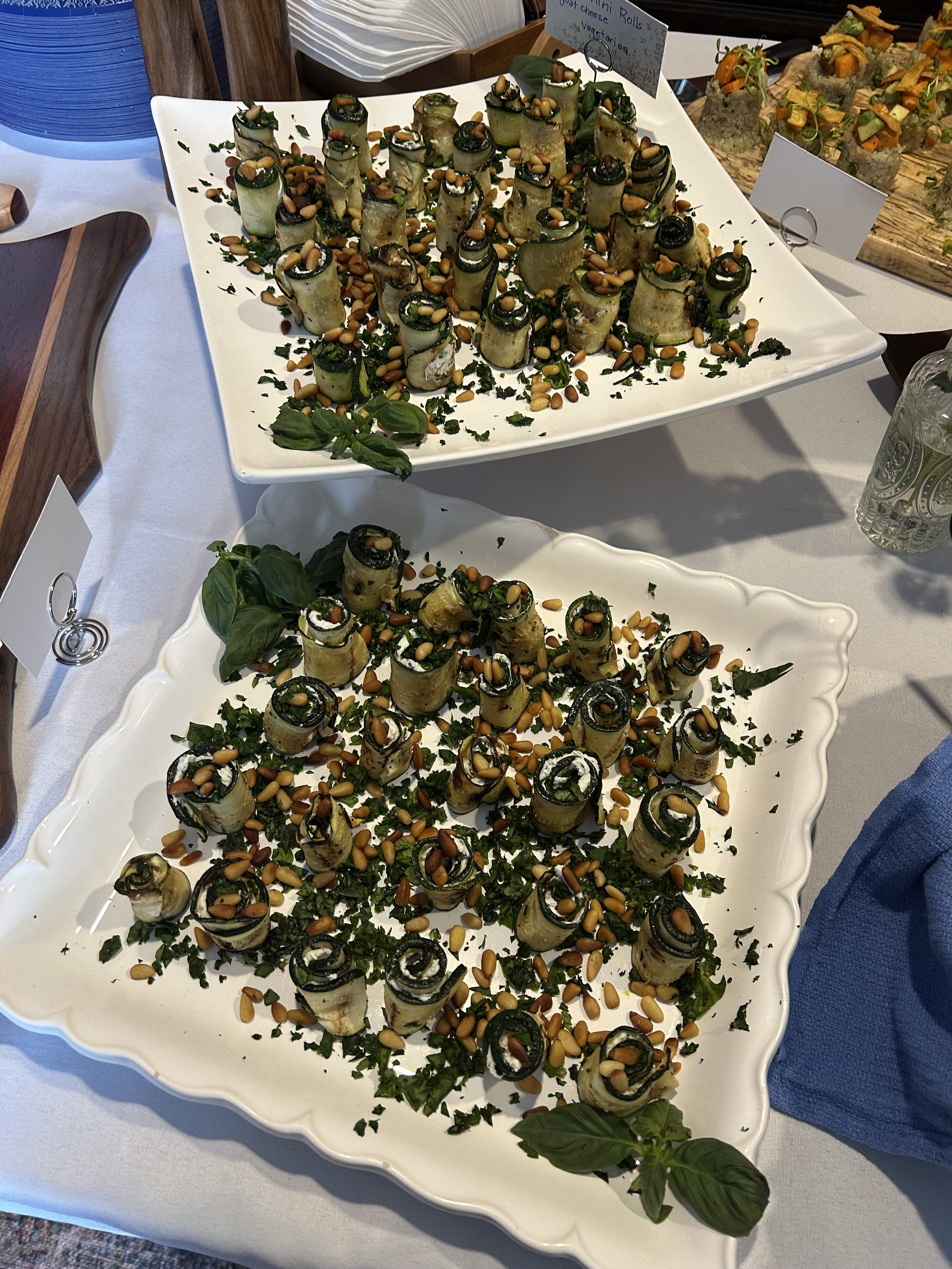 Plate of rolled vegetable appetizers garnished with pine nuts, herbs, and green leaves.