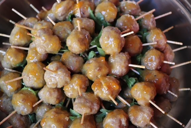Close-up of small meatballs with toothpicks, garnished with green herbs, on a tray.