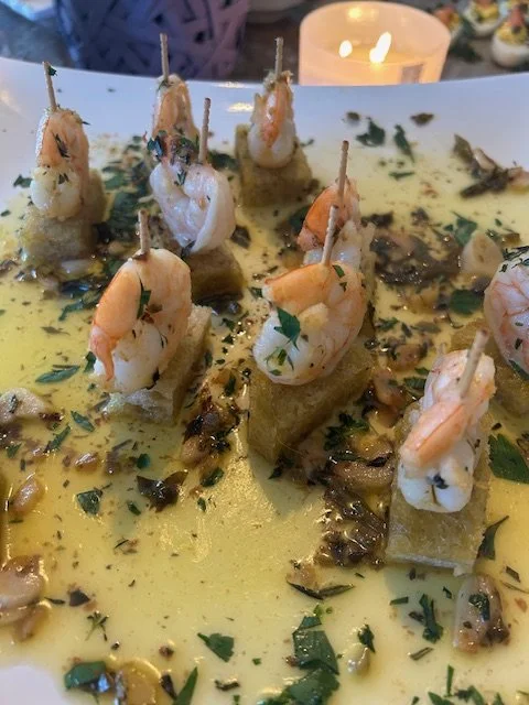 Appetizer with shrimp on top of bread, garnished with chopped herbs and seeds, served with a butter or oil-based sauce.