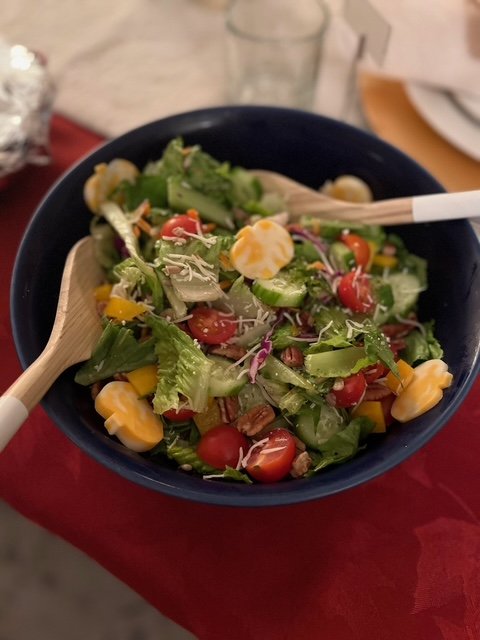 Bowl of mixed salad with cherry tomatoes, chopped lettuce, corn, and shredded cheese, with wooden salad tongs.