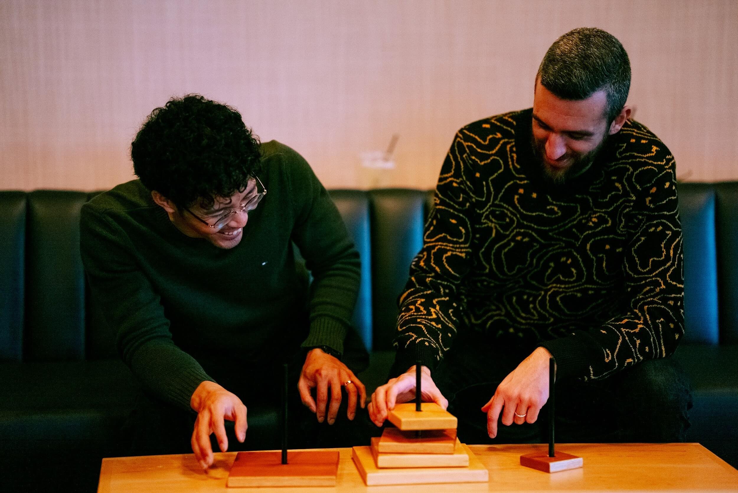Two co-workers laugh while figuring out the Tower of Hanoi game