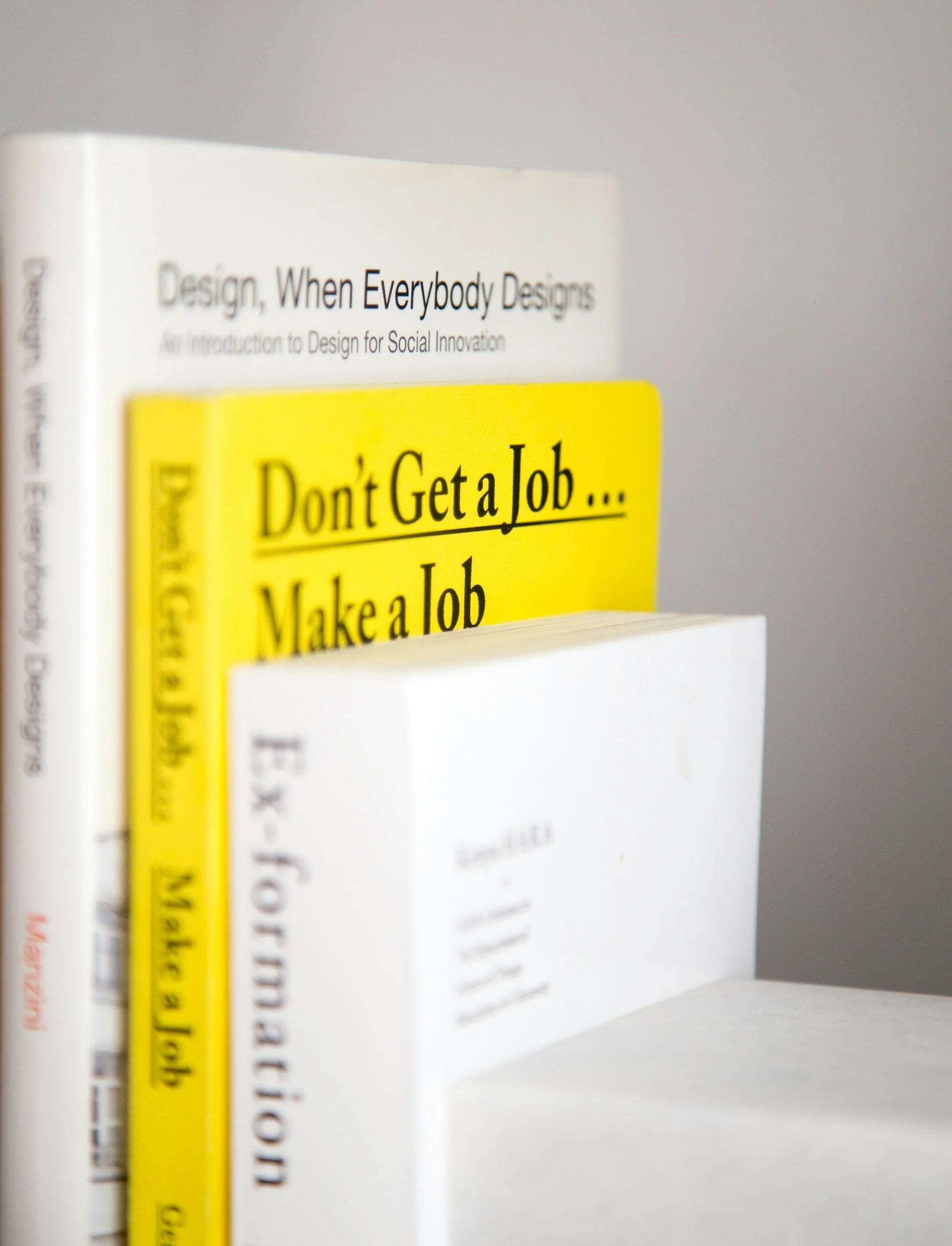 Close-up of three books stacked, with the middle one titled 'Don't Get a Job... Make a Job' in bright yellow, and the others partially visible, including 'Design, When Everybody Designs'.