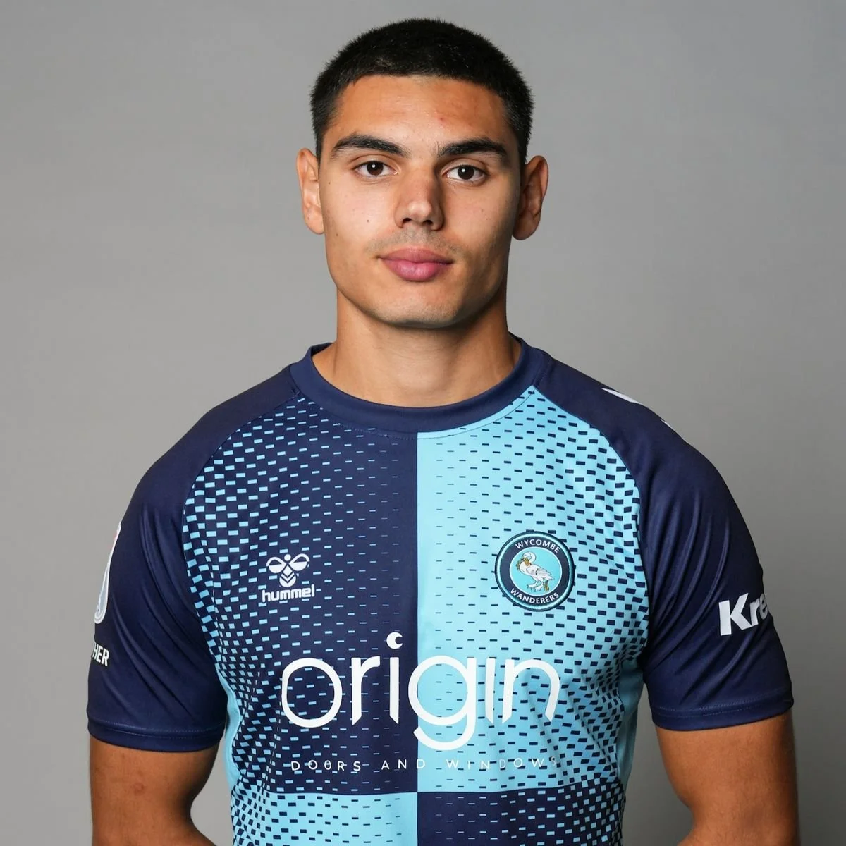 Portrait of a young male soccer player in Wycombe Wanderers jersey against plain gray background.
