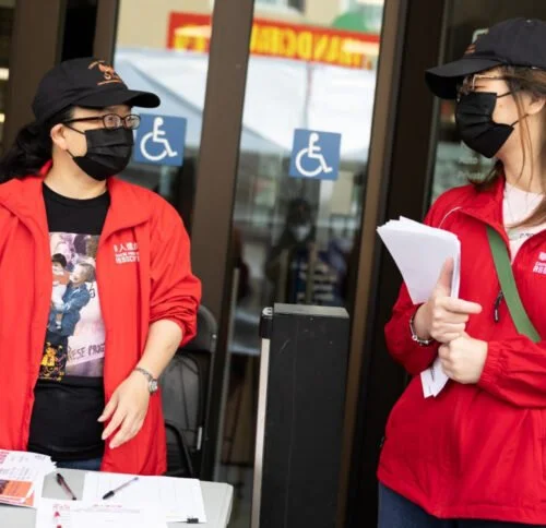 Two CPA activists stand outside, holding papers.