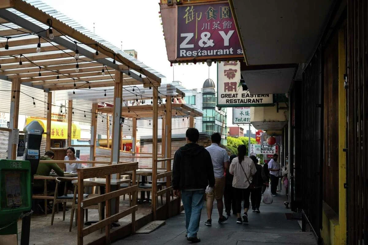 People walking on a side walk beside a parklet.