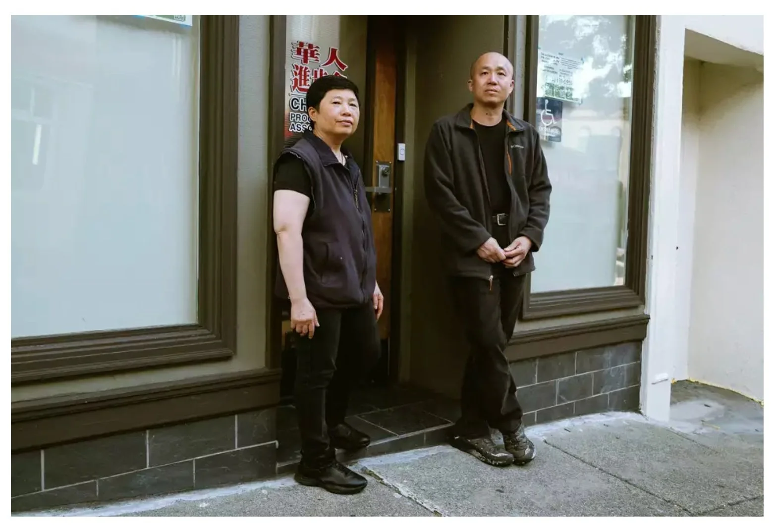Two people stand in front of an office door.