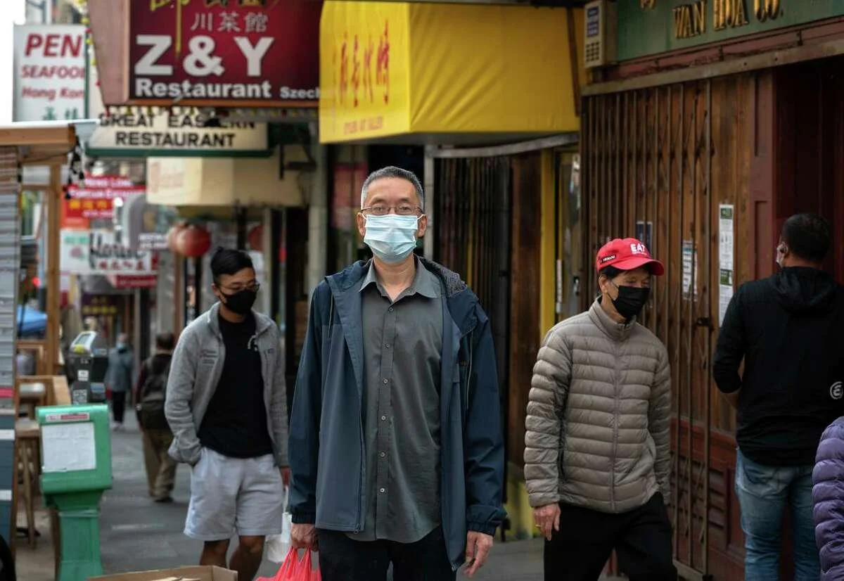 A man with a face mask standing on the sidewalk.