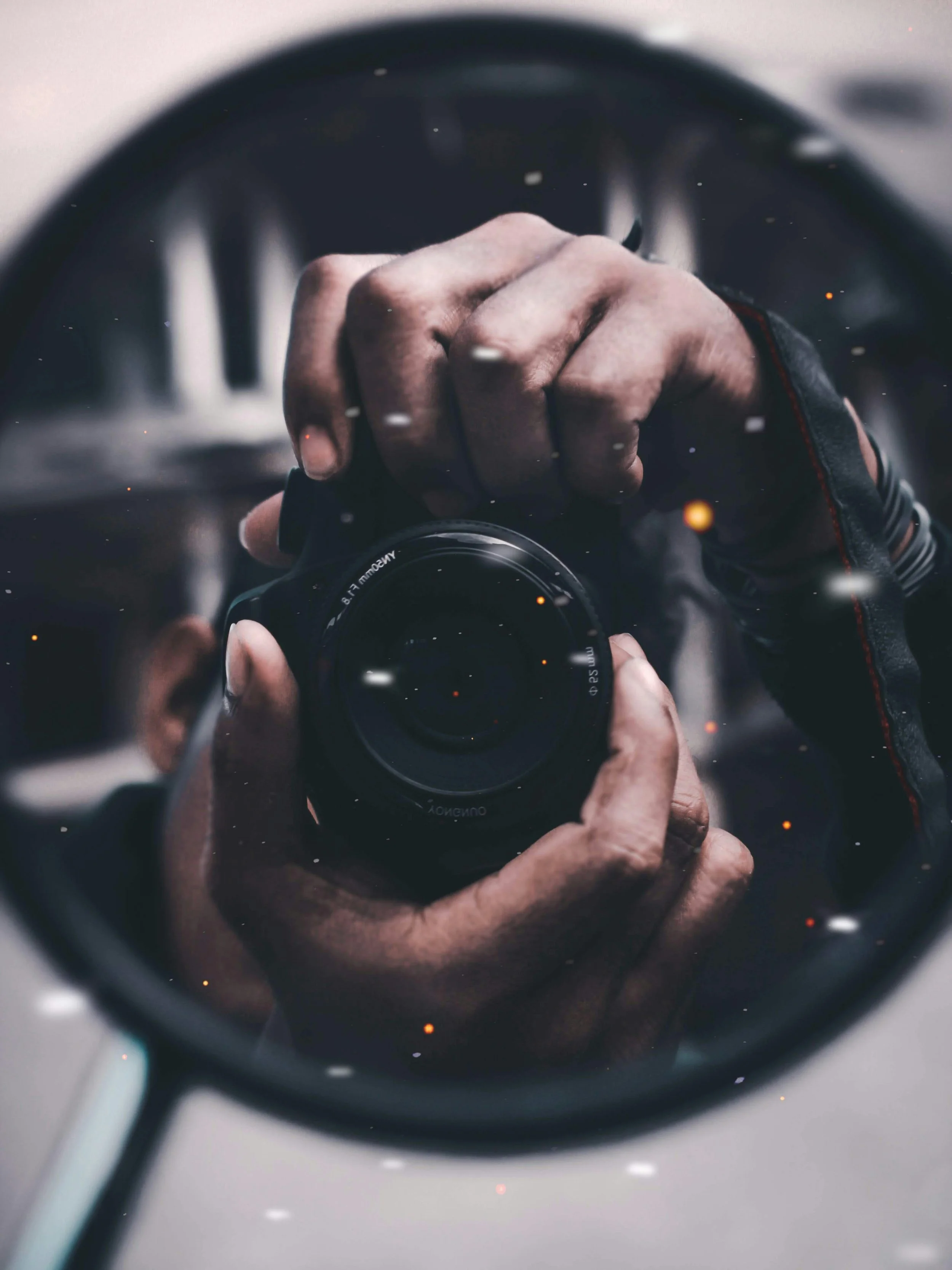 A person taking a photo of themselves using a camera, reflected in a mirror or a shiny surface, with a focus on the camera lens and their hand.