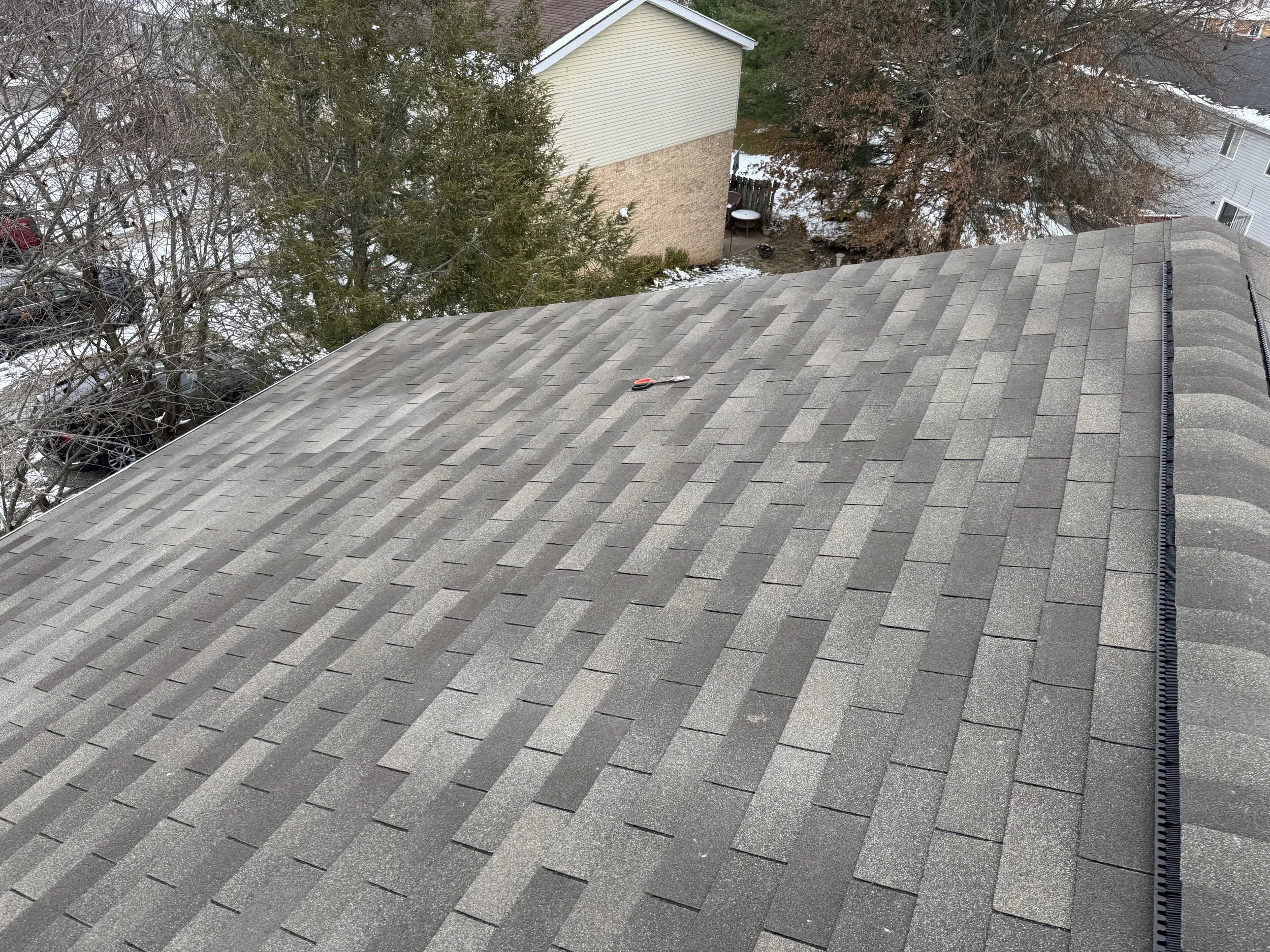 View of a rooftop with gray asphalt shingles, a pair of pliers resting on it, and a gutter on the right edge.