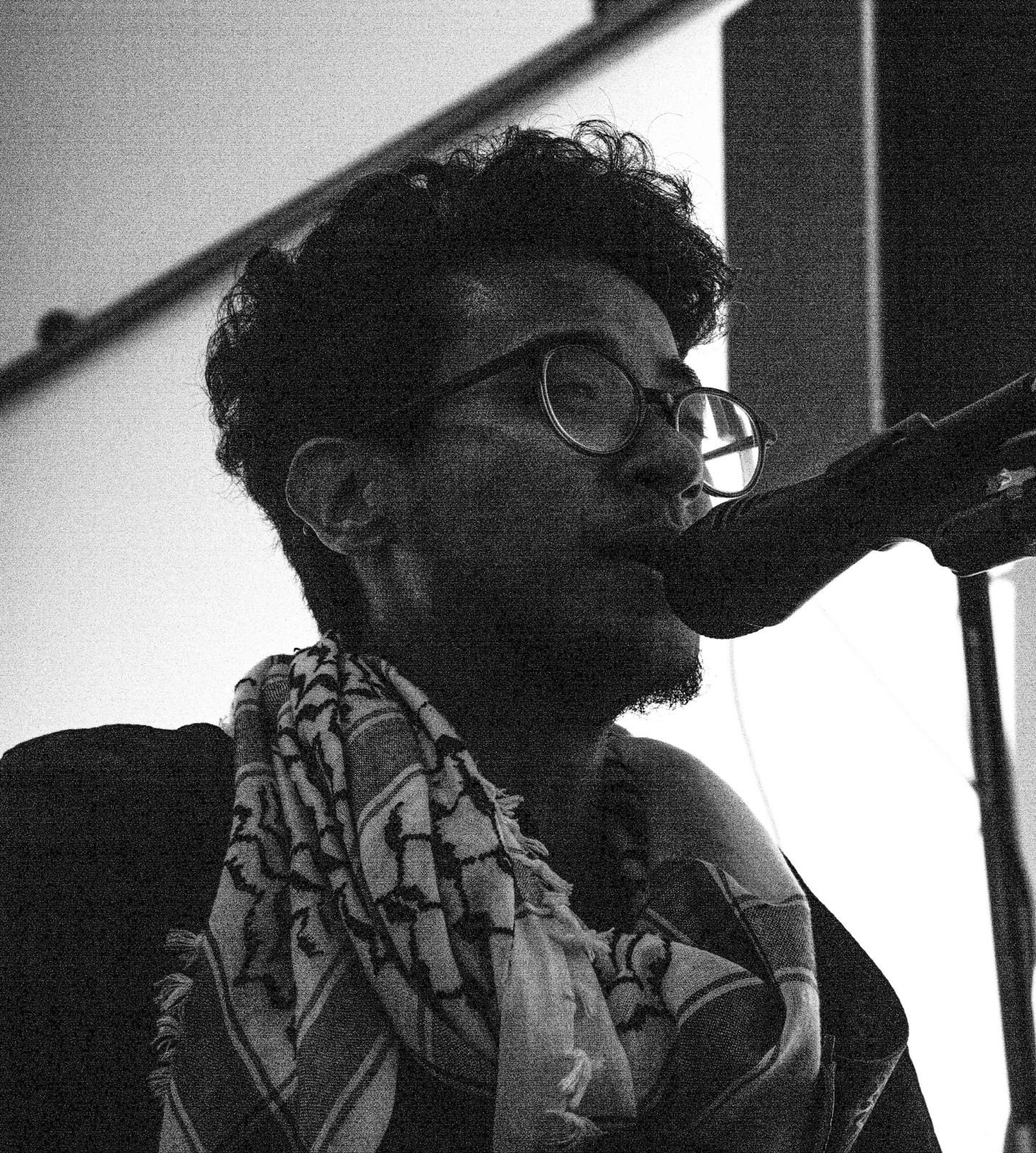 Eros Miguel Luz with glasses singing into a microphone, wearing a patterned scarf and a jacket, in a black and white photograph. JAHA Film Festival closing gala.