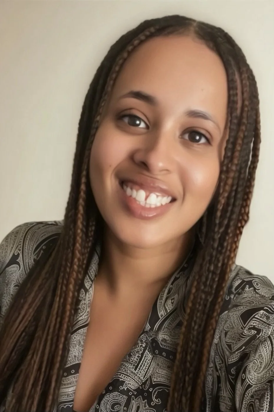 A young woman with braided hair and a patterned top, smiling at the camera against a plain background.