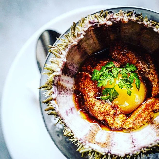 A baked sea urchin with an egg and herbs inside, served in its shell.