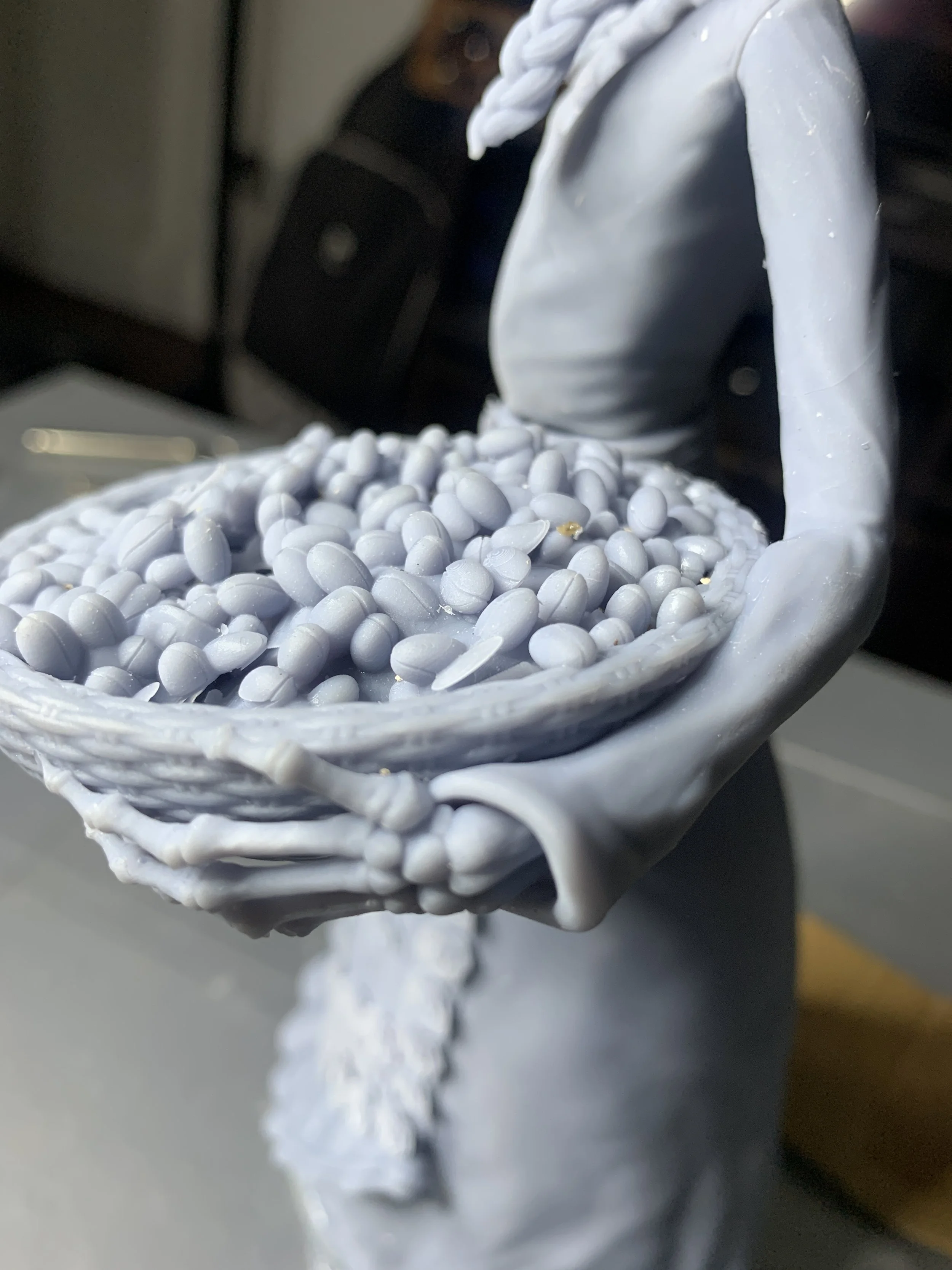 Close-up of a 3D-printed figure holding a basket filled with small round objects.