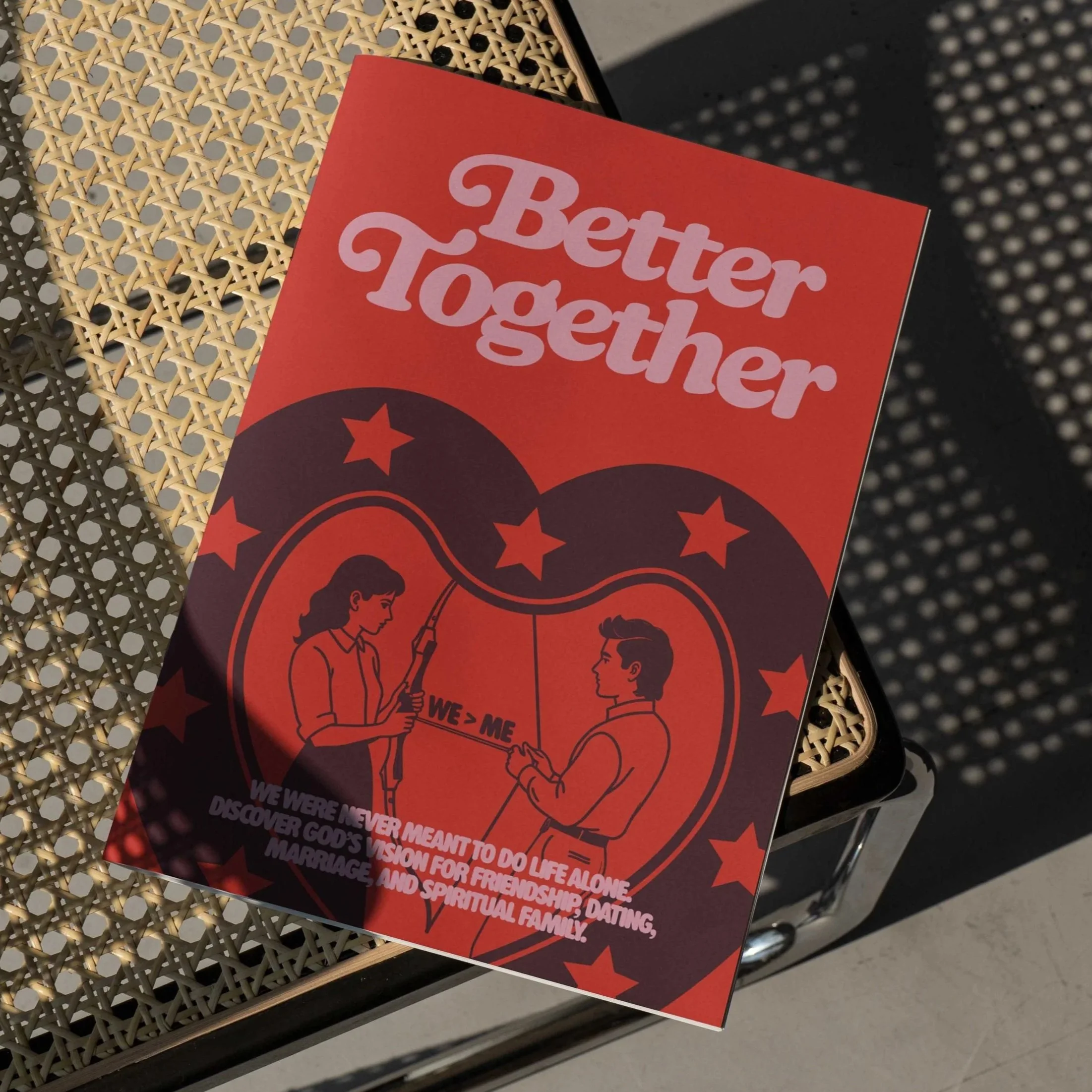 Smartphone screen displays a message screen with an inspirational quote, "See you tomorrow," and prayer times for 9 am and 11 am. In the background, a church steeple with a cross is partially visible, parked next to an open book with dense text, possibly a Bible. The scene appears to be outdoors on a sandy surface.