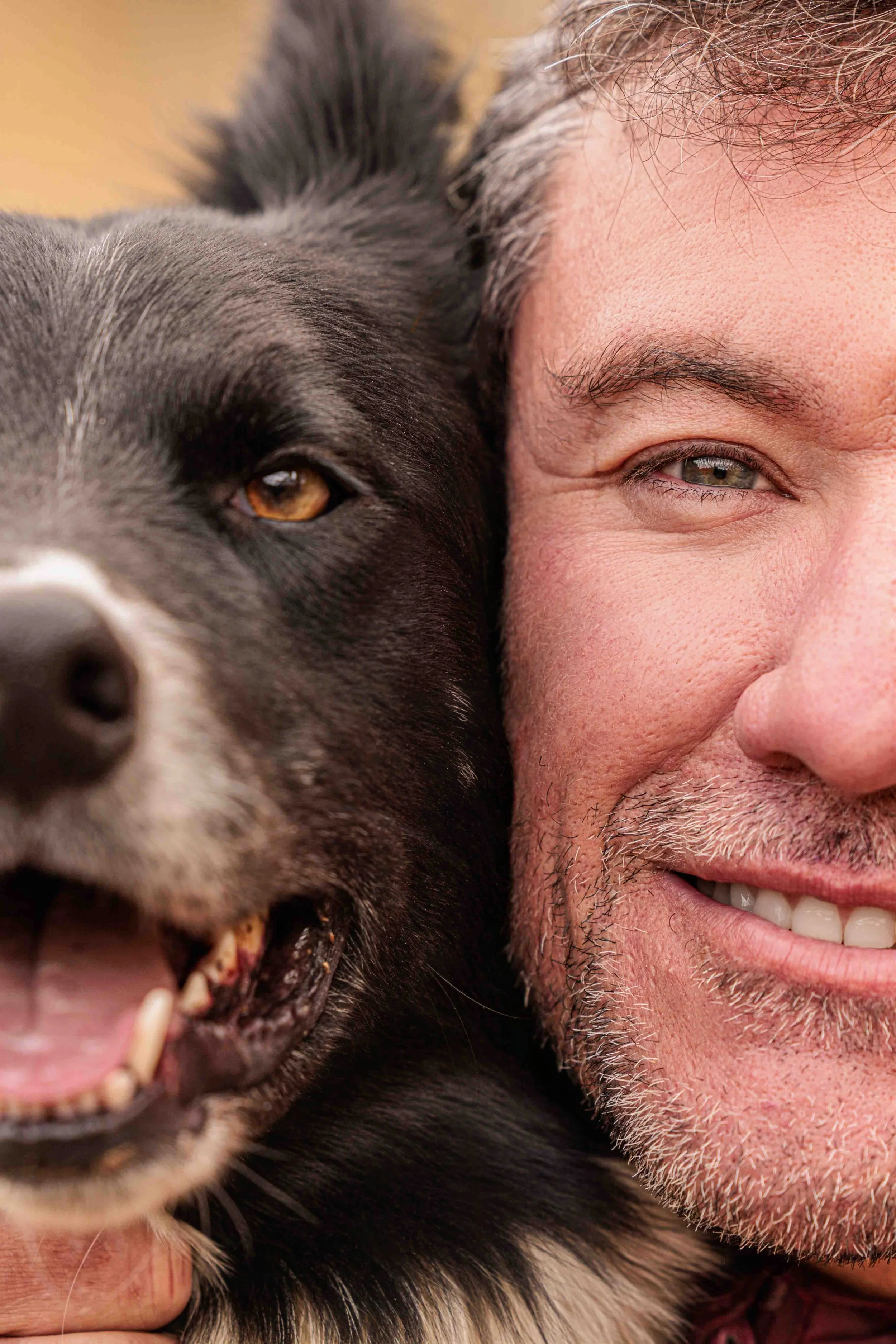 Close-up of a man smiling with his face close to a black and white dog, both looking at the camera.
