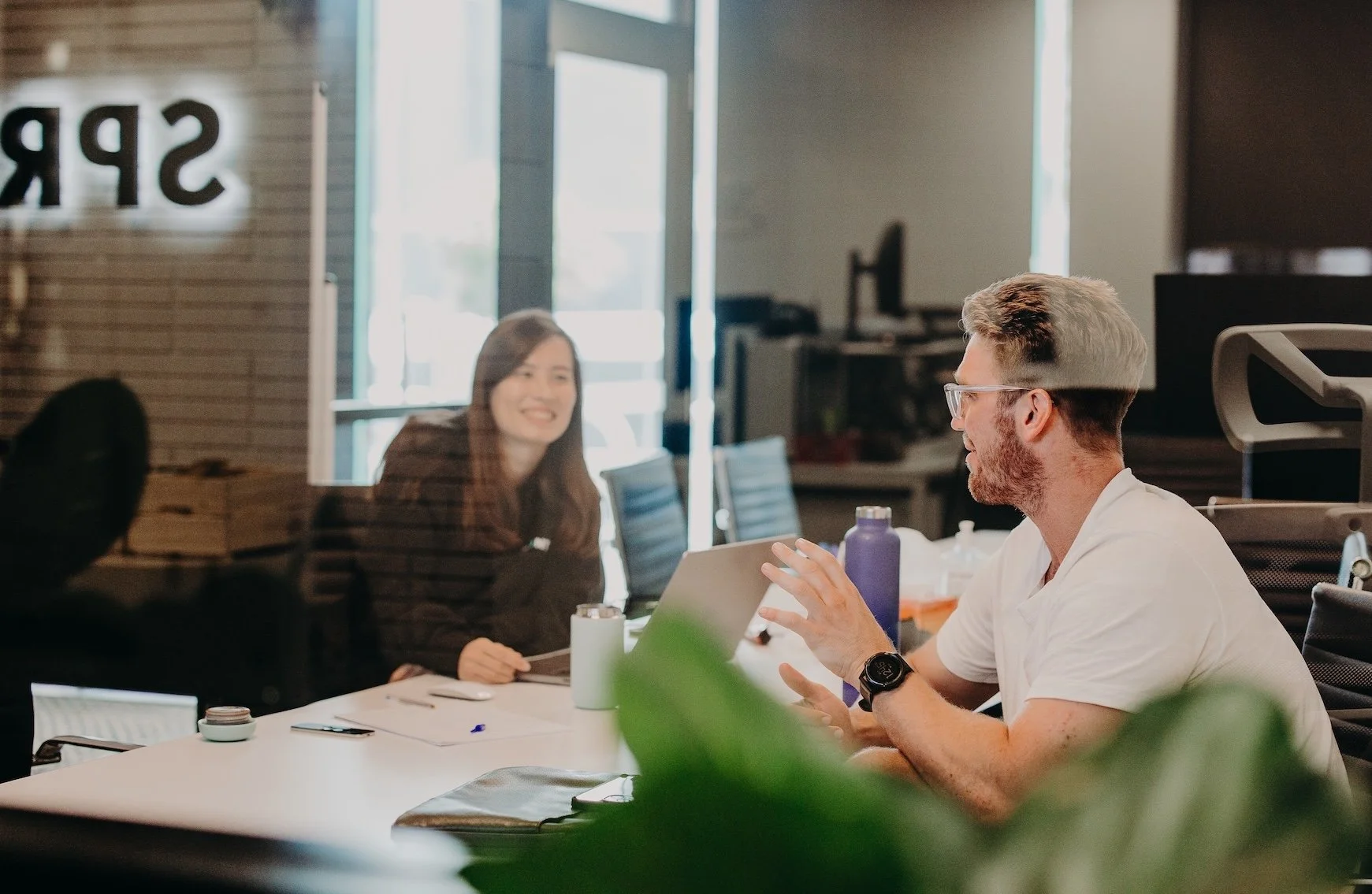 Two people in a meeting room, laughing and talking.