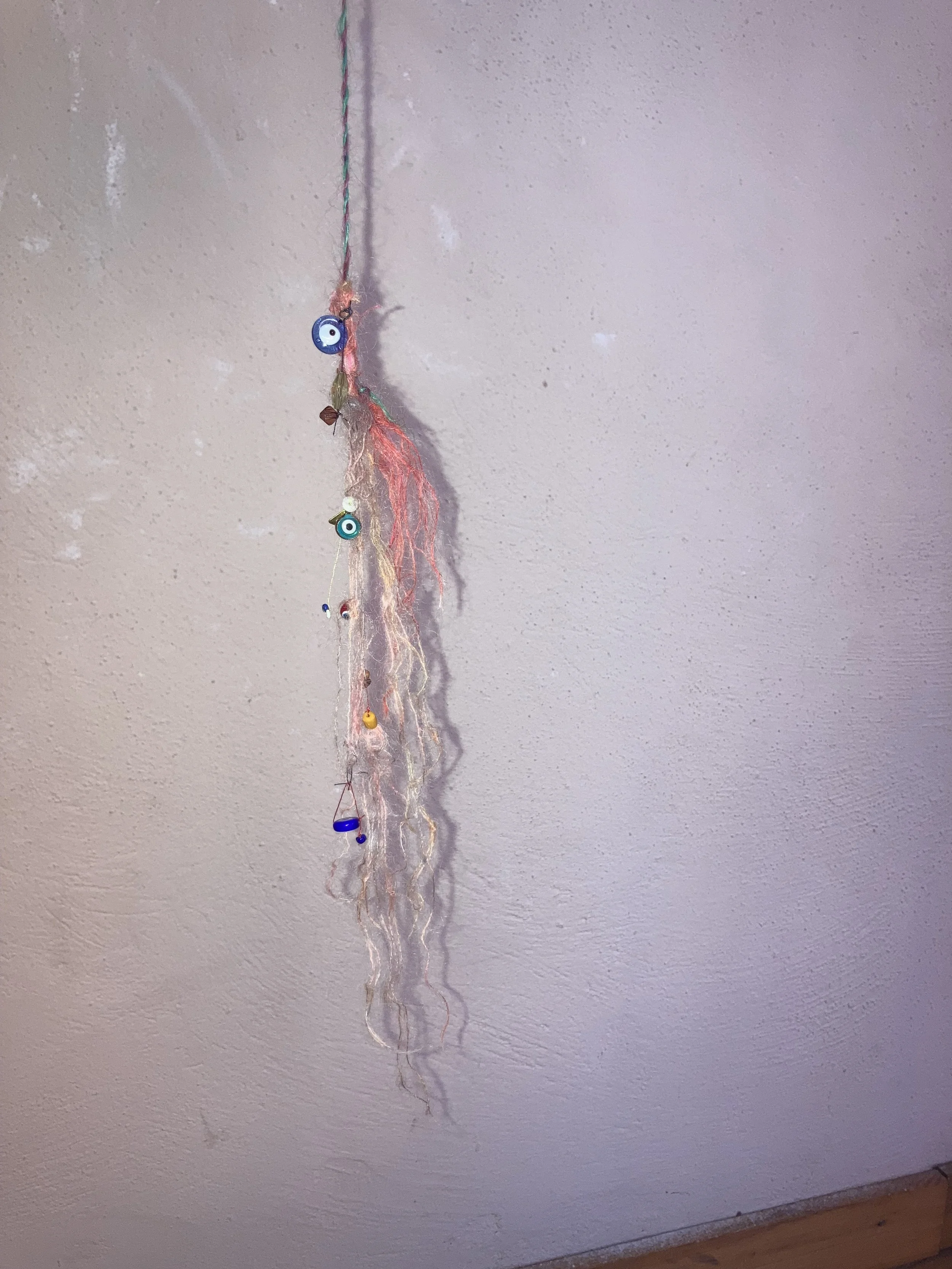 Une décoration suspendue faite de ficelle, perles et yeux de sorcière, accrochée à un plafond blanc.