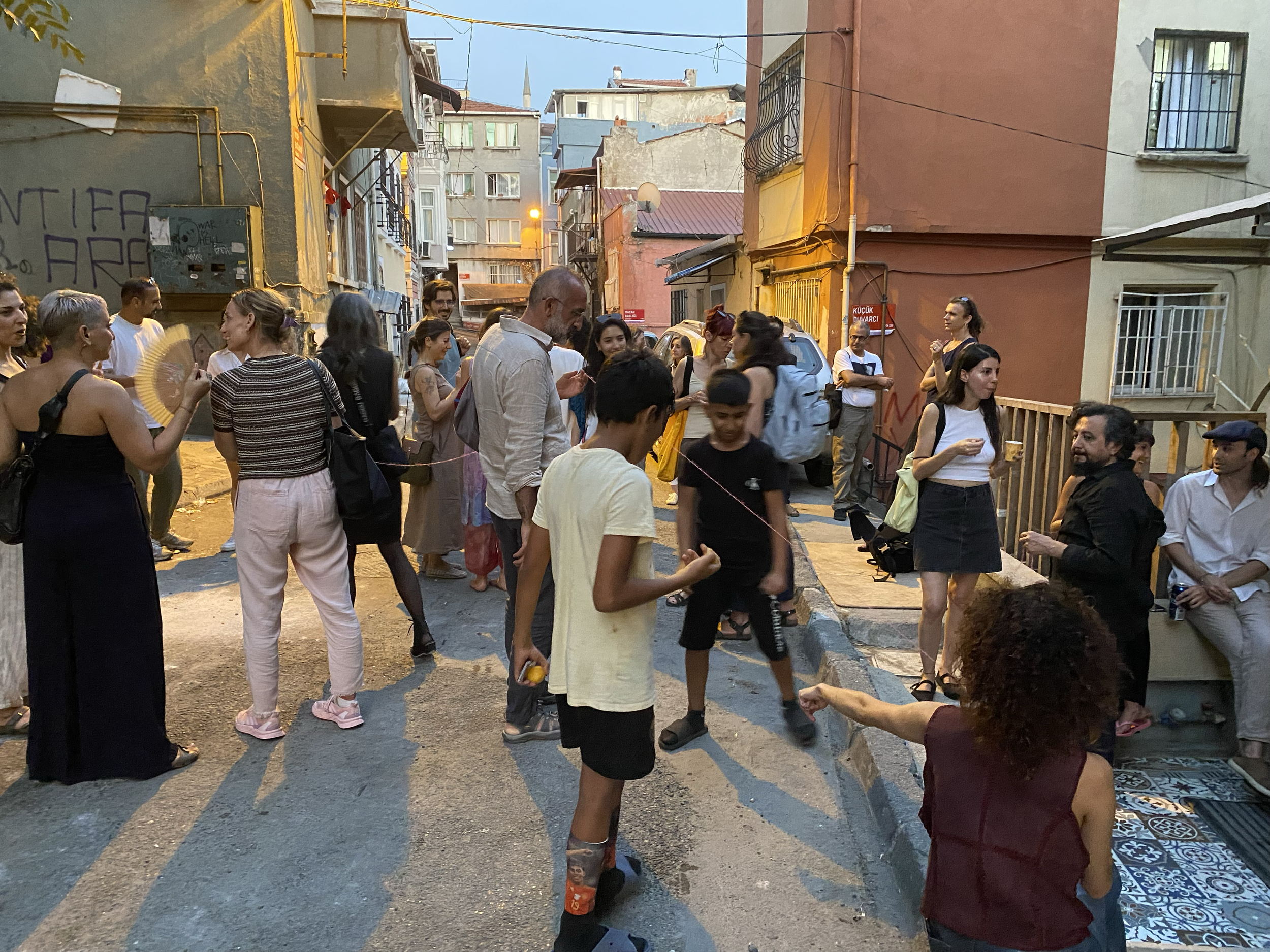 Groupe de personnes socialisant dans une rue urbaine en soirée avec bâtiments colorés.