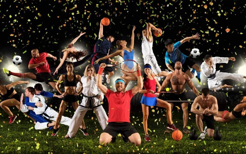 Group of athletes and sports enthusiasts posing with various sports equipment in a stadium with a dark background and golden confetti, including soccer balls, footballs, a volleyball, a tennis racket, and kettlebells.