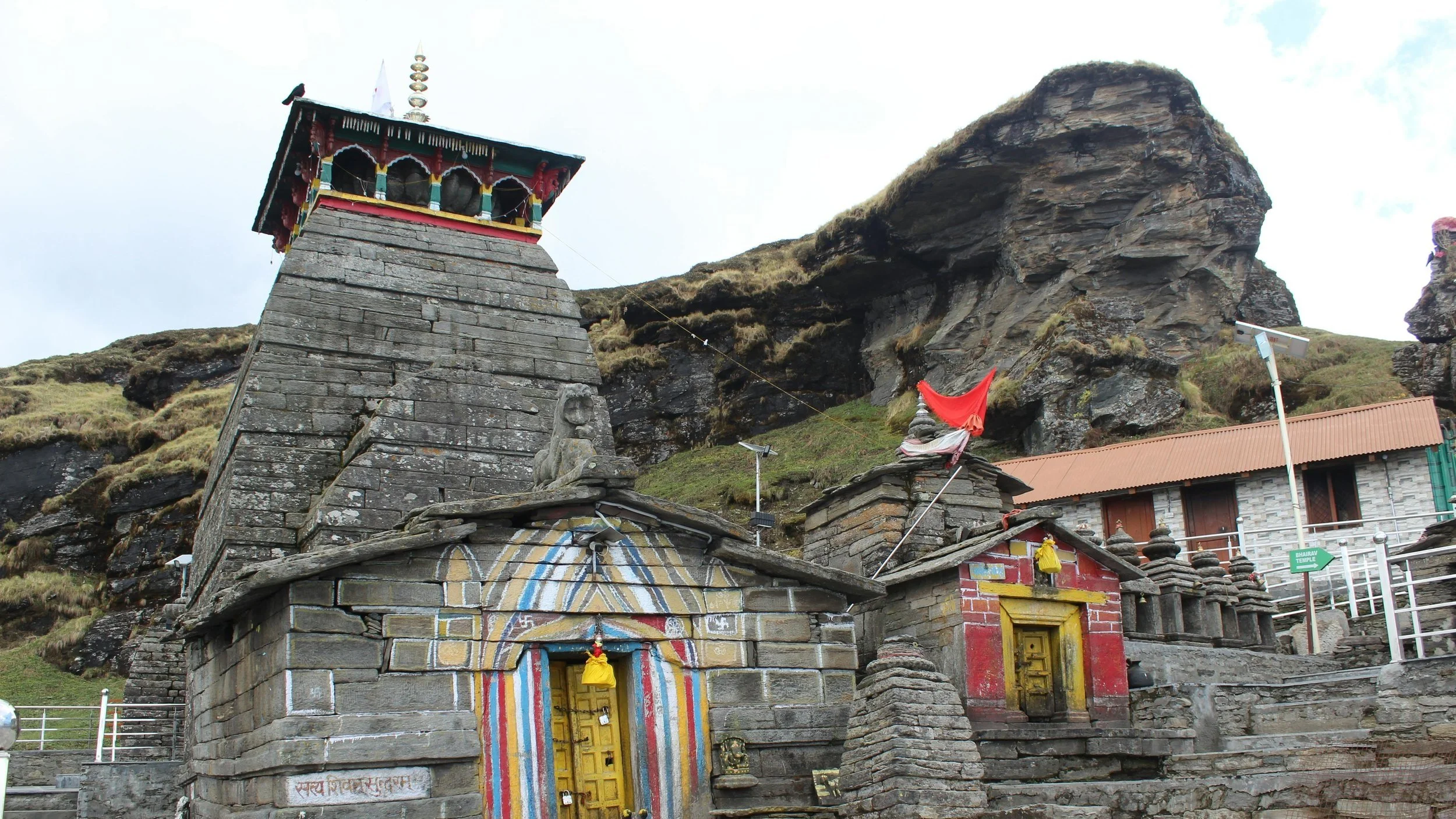 Stone temples with colorful doorways and flags, set against a rocky hillside.
