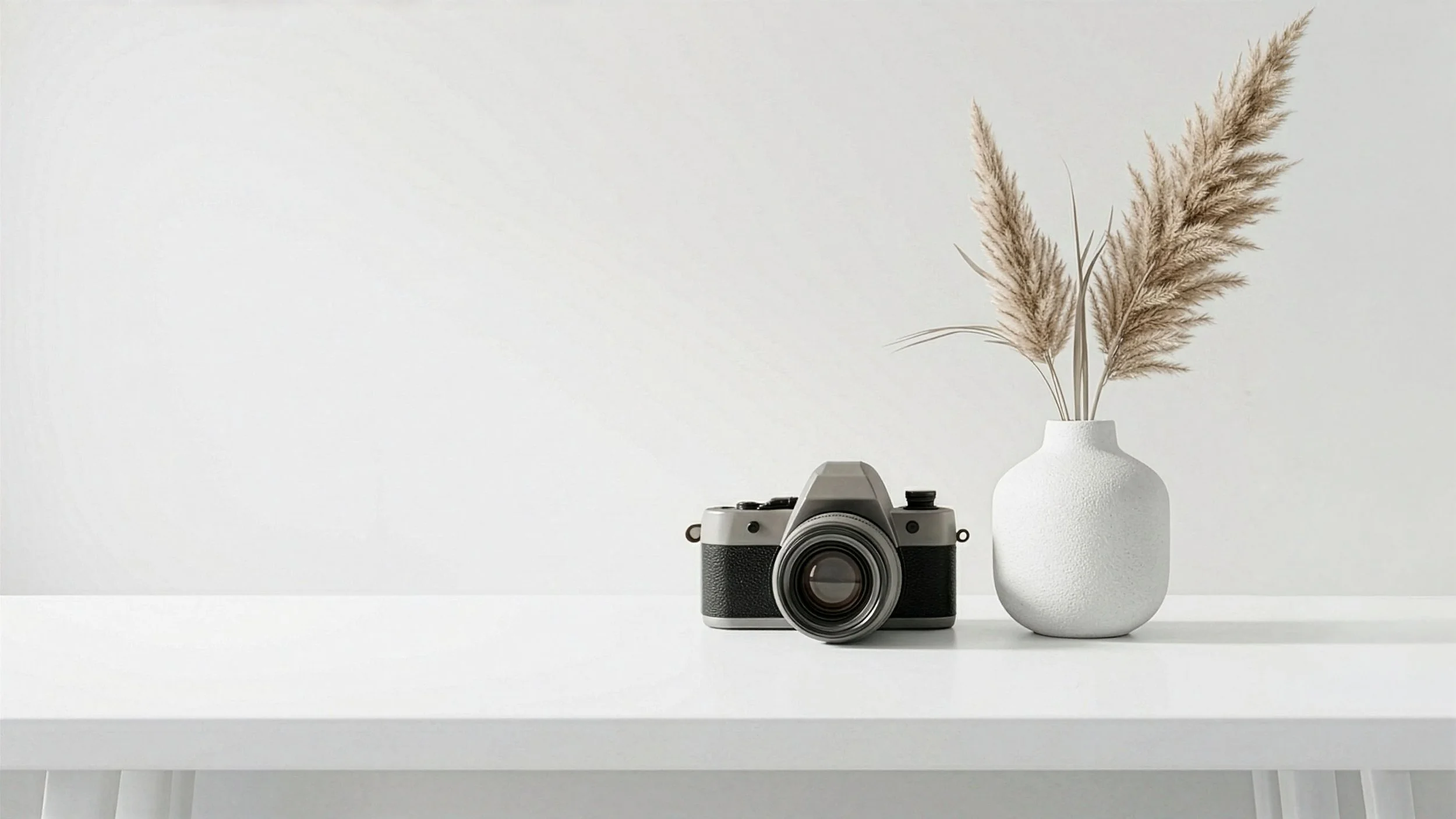 Une table blanche avec un appareil photo vintage contre un mur blanc minimaliste, symbolisant la vision de la direction artistique par Mathilde Lafargue