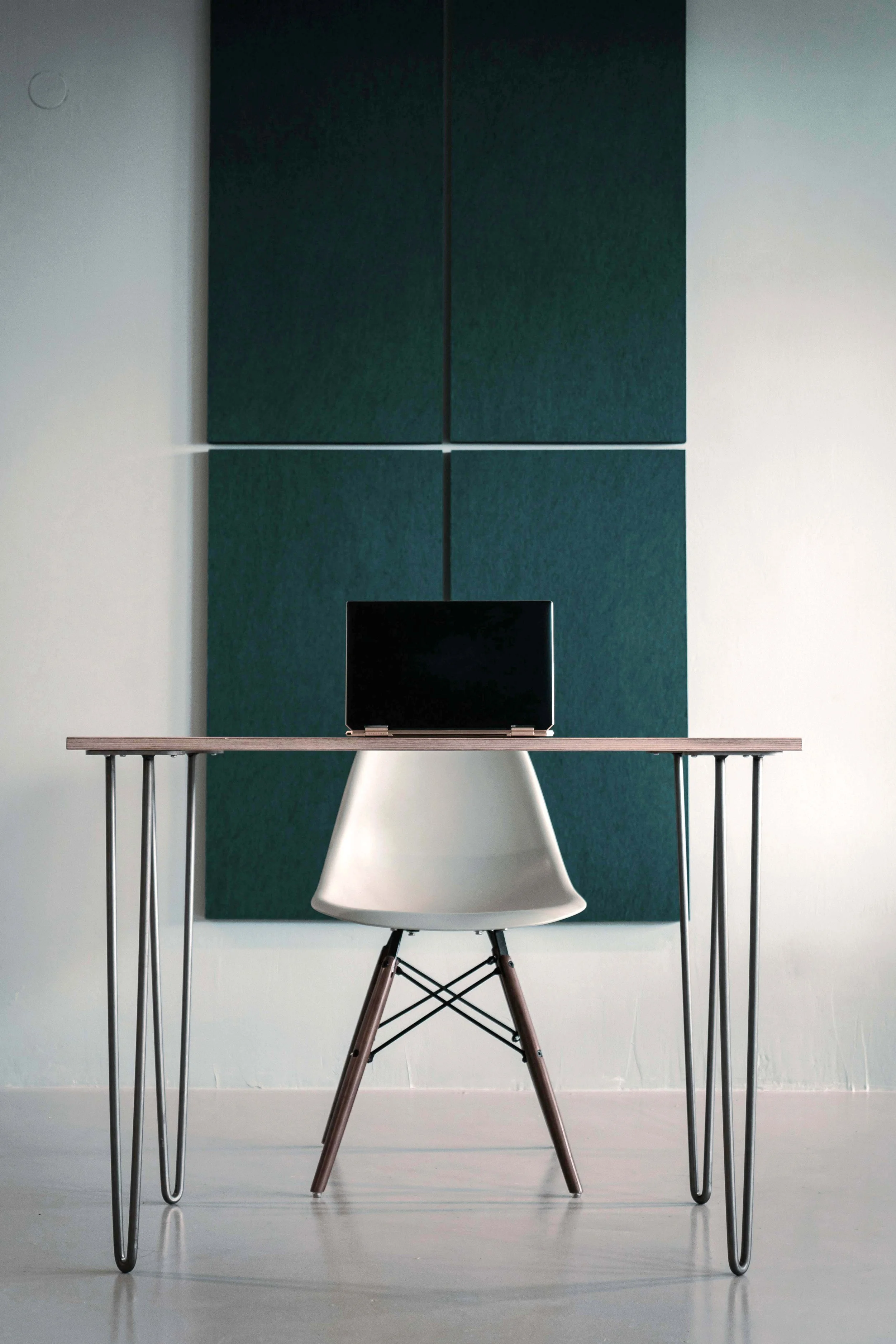 Un bureau avec une chaise blanche, un ordinateur portable noir ouvert, une table en bois léger, et un mur avec des panneaux acoustiques verts.