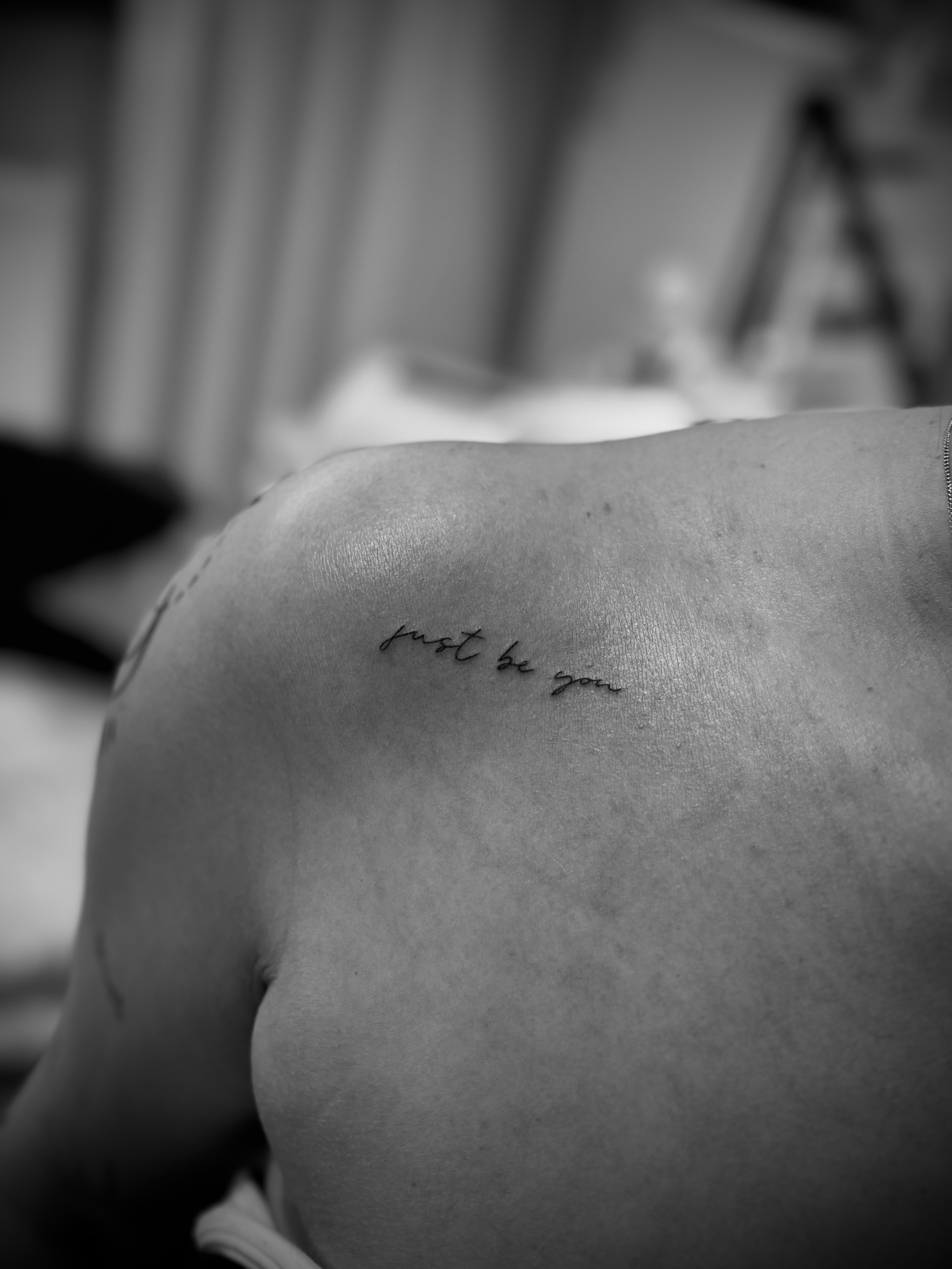 Black and white photo of a person's shoulder with a tattoo reading "just be you."