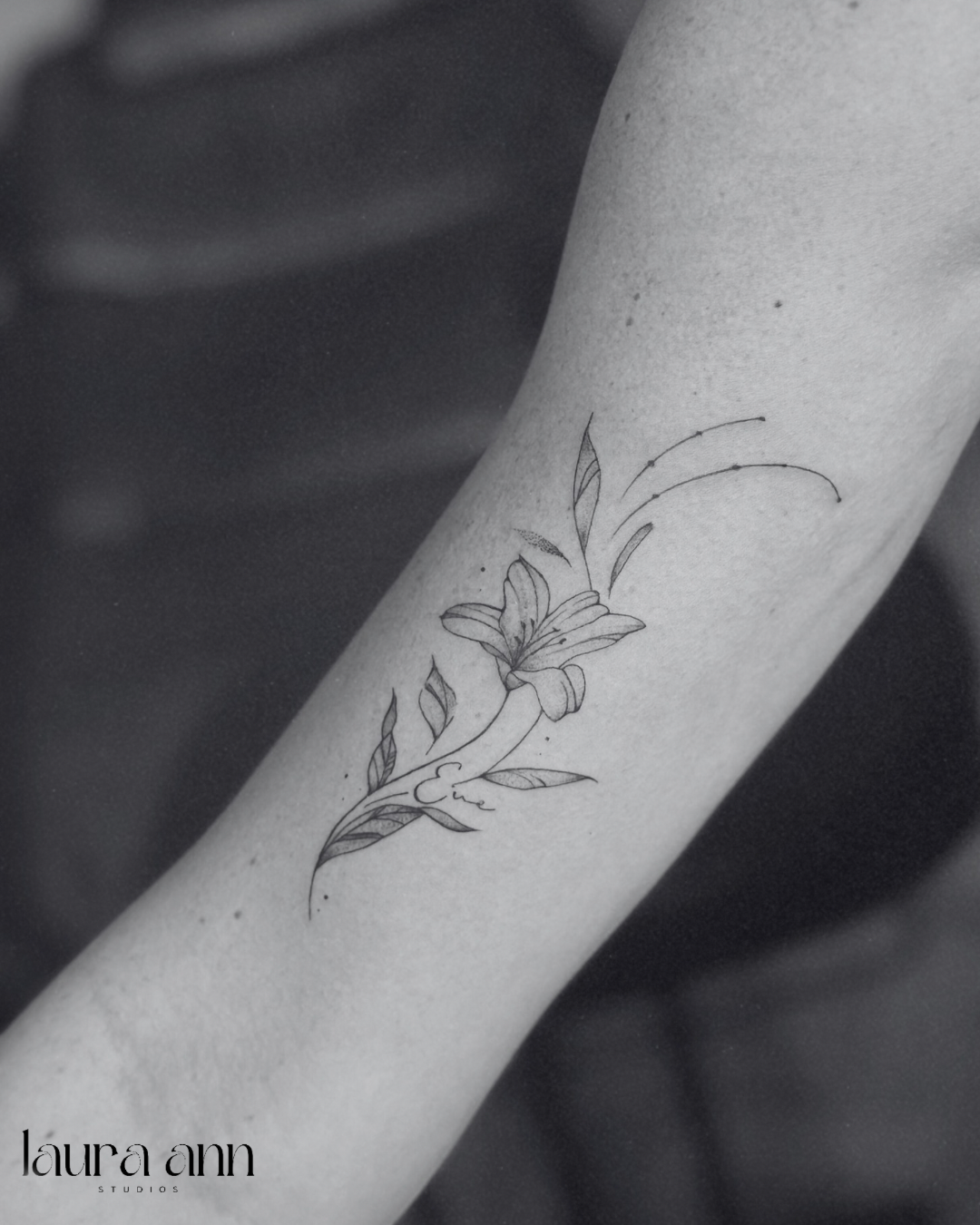 Tattoo of a lily flower with leaves on an arm.