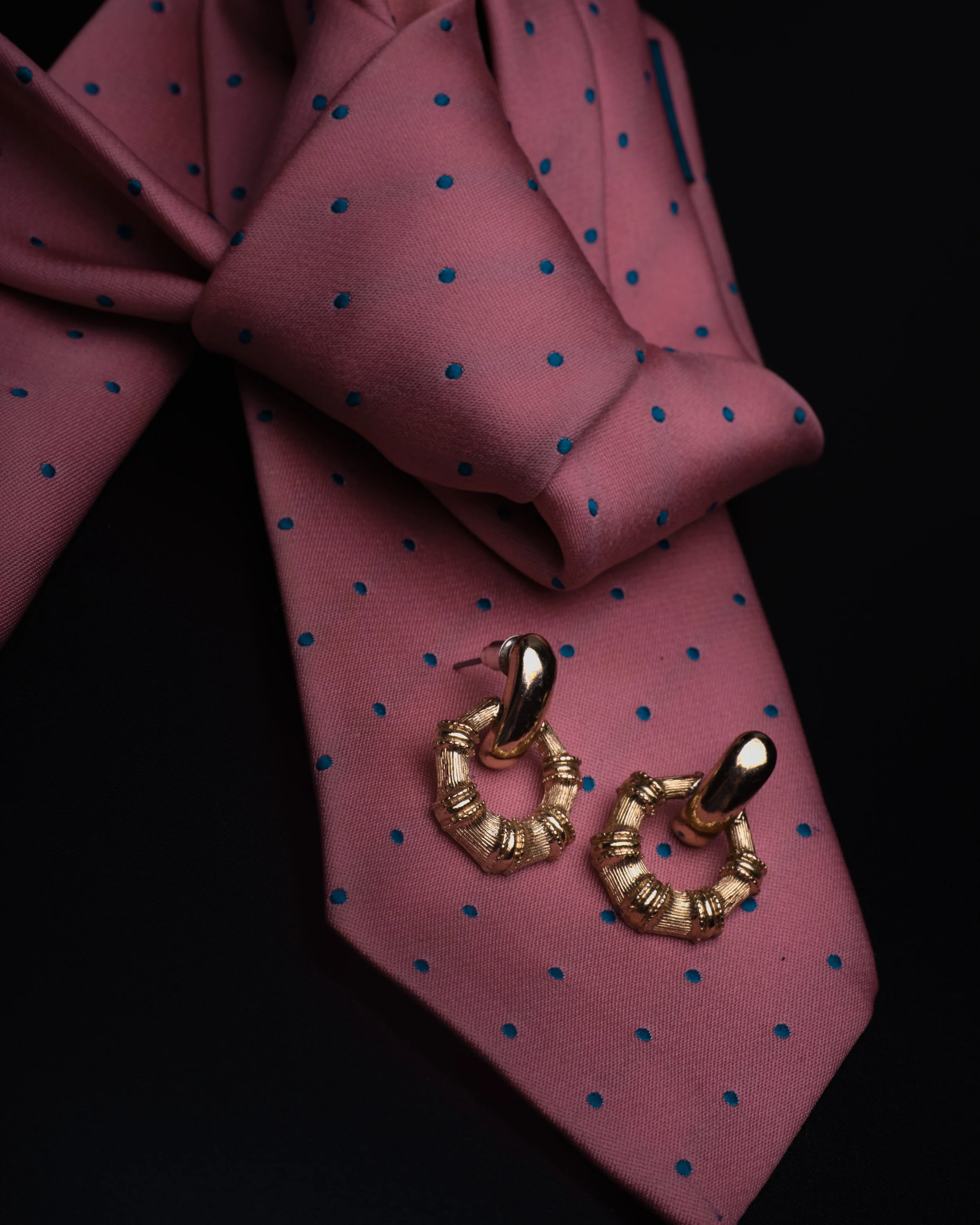 Close-up of pink fabric with blue polka dots, a gold-colored jewelry piece, positioned on a dark background.